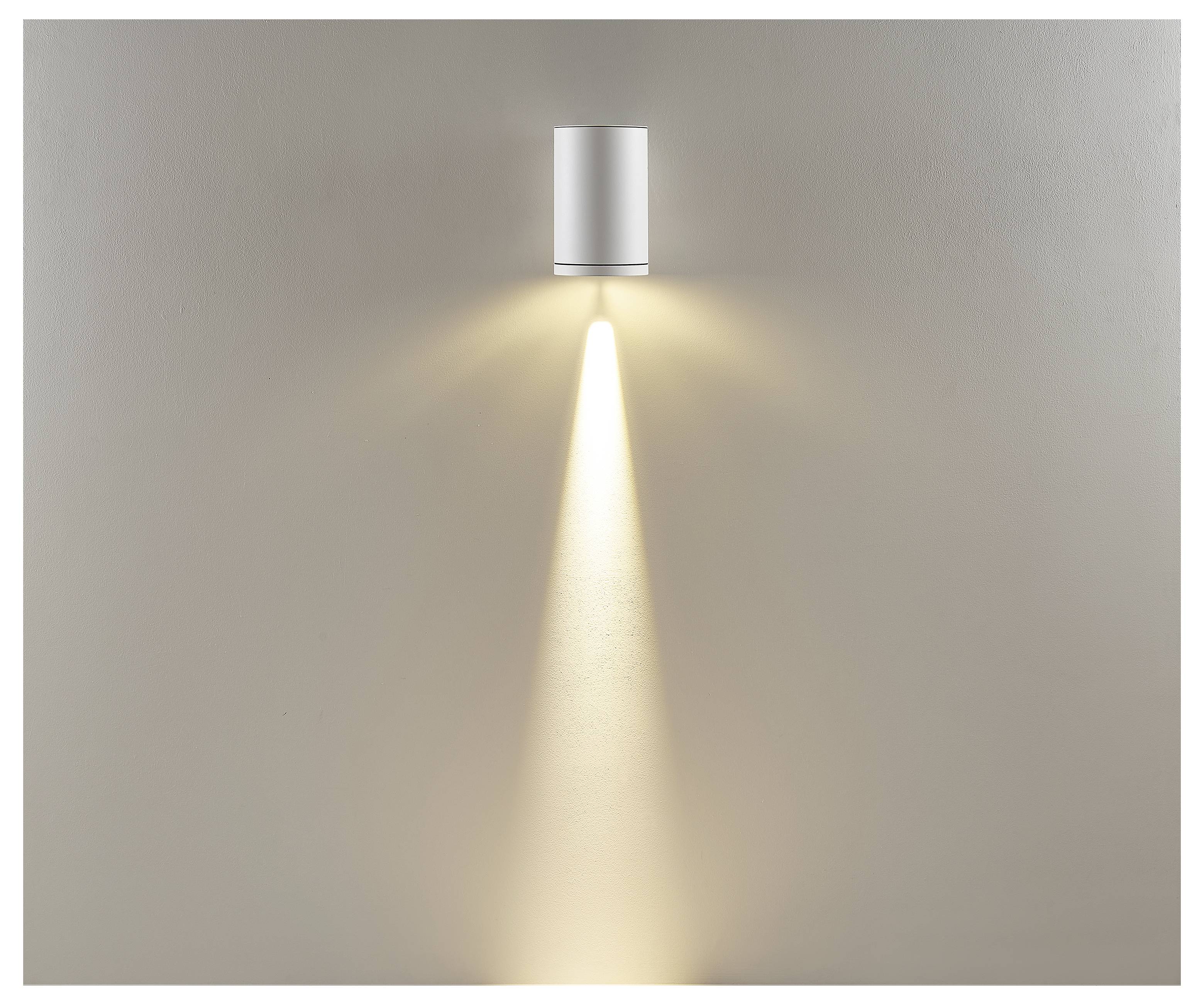 An der Wand montierte zylindrische Leuchte, die einen engen Lichtstrahl nach unten auf eine beige Wand wirft.