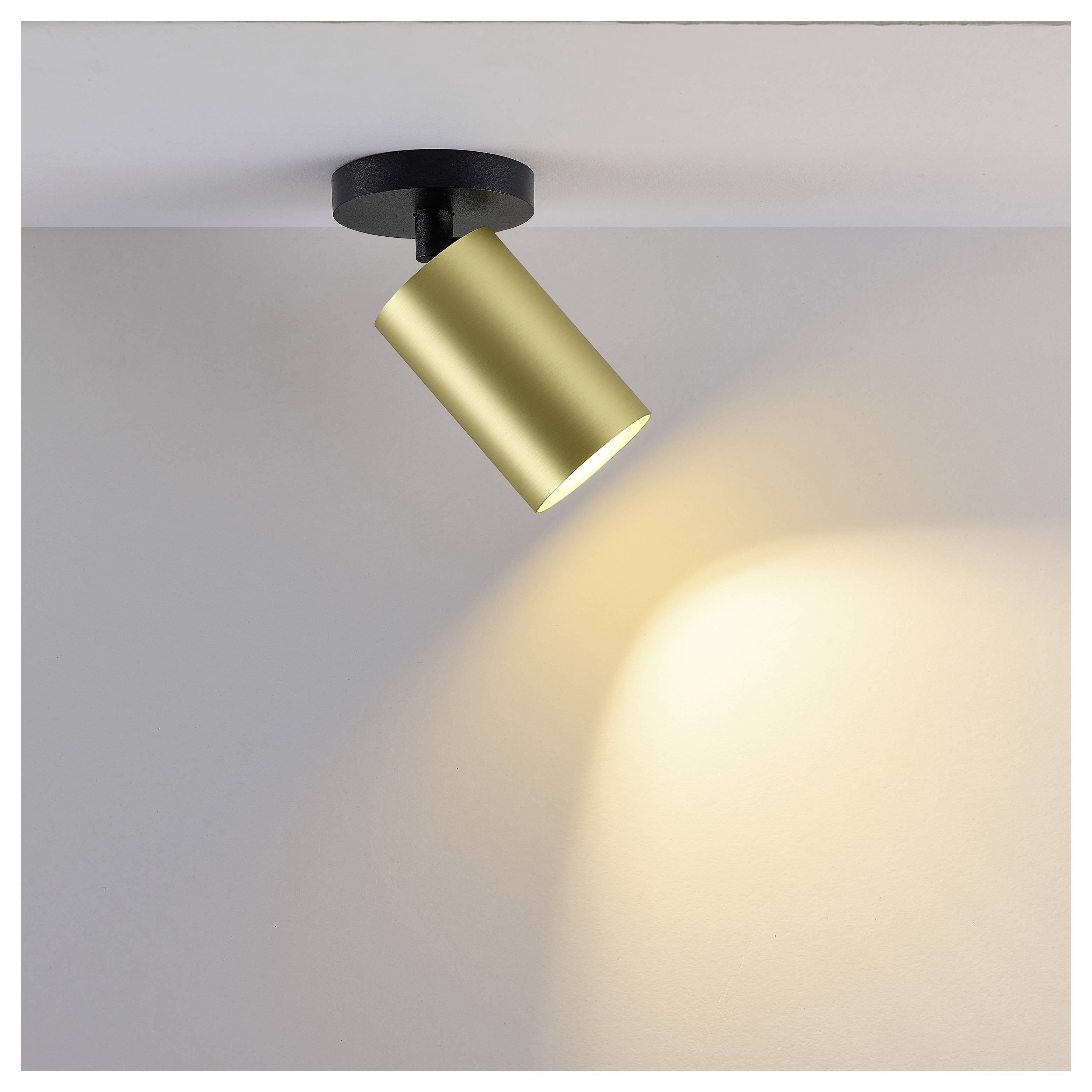 Goldener Deckenspot, der warmes Licht auf eine schlichte Wand wirft.