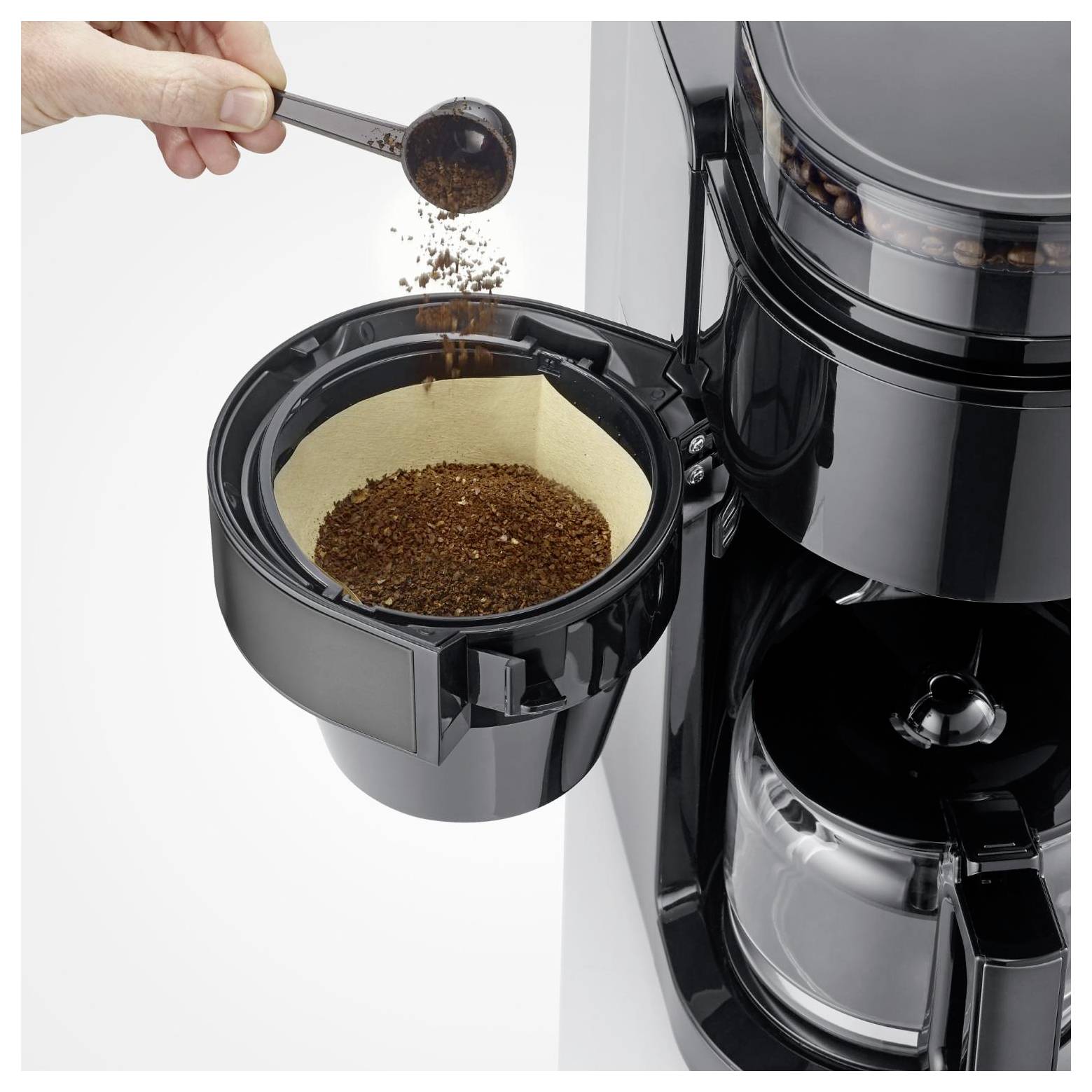 Eine Hand gießt gemahlenen Kaffee in den offenen Filterkorb einer Kaffeemaschine, bevor das Brühen beginnt.