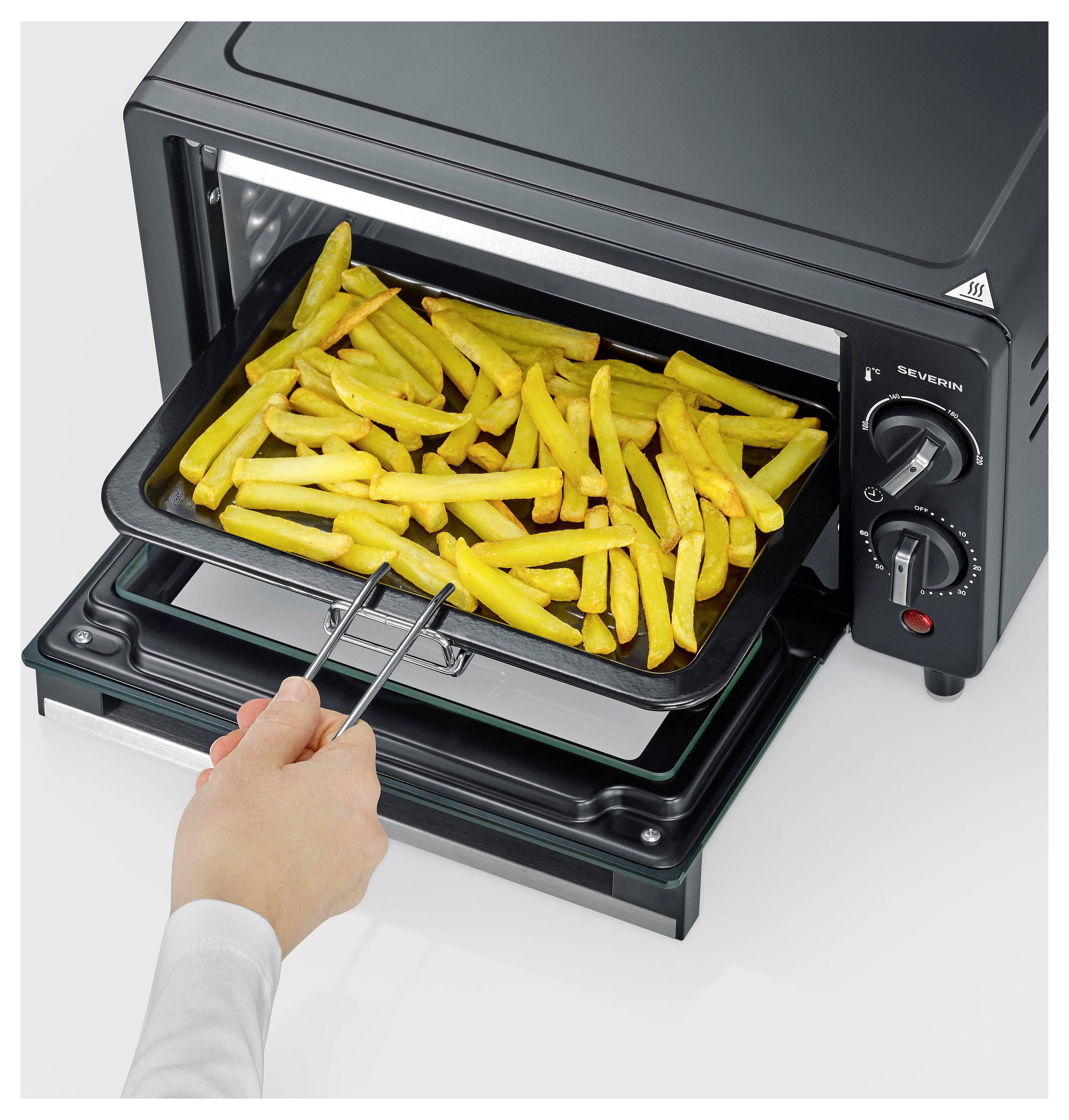 Hand entfernt ein Tablett mit gekochten Pommes Frites aus einem kleinen Arbeitsplatten-Ofen oder Toasterofen.