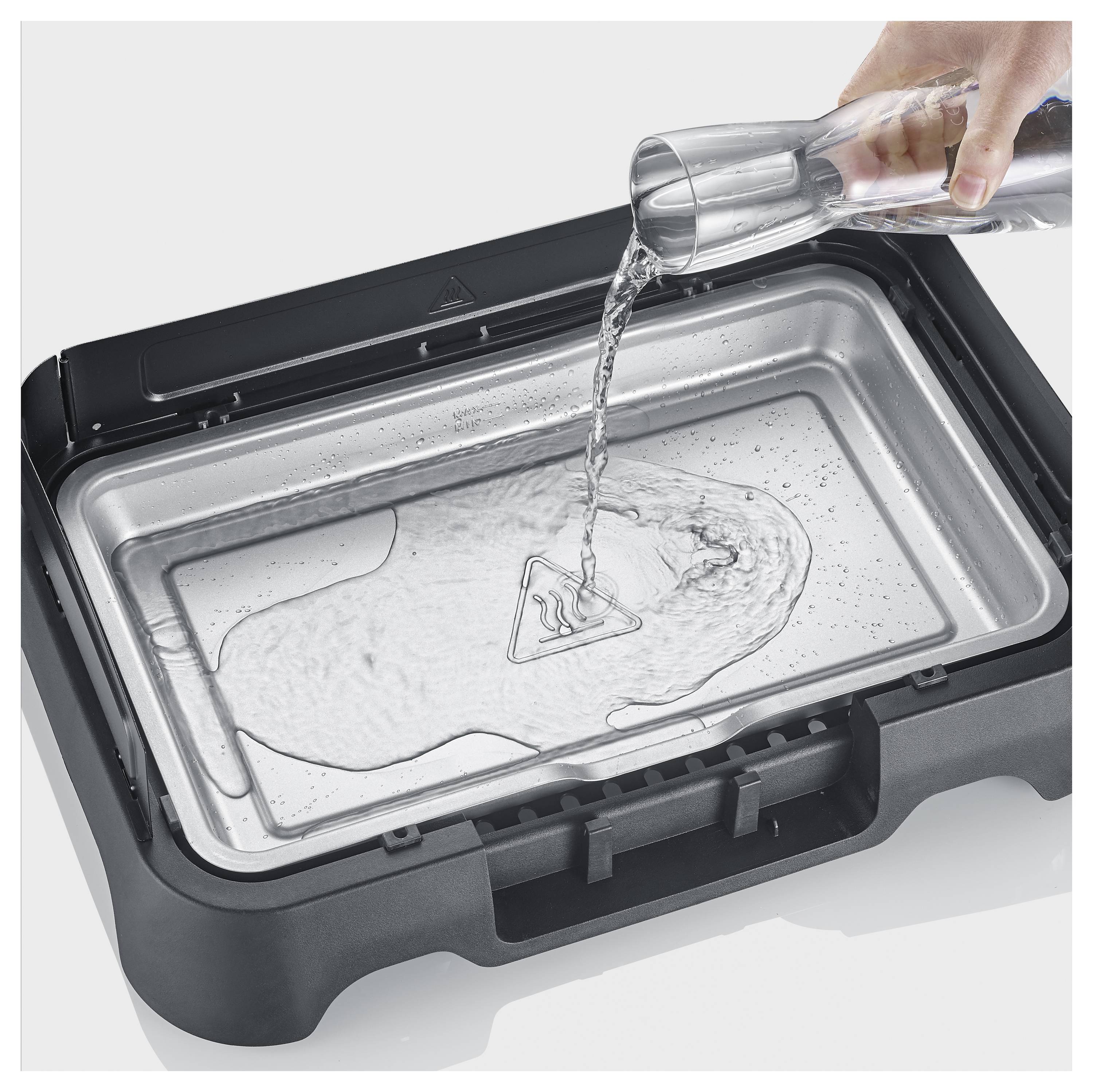 Hand gießt Wasser in einen offenen elektrischen Grill oder Sandwichmaker zum einfachen Reinigen