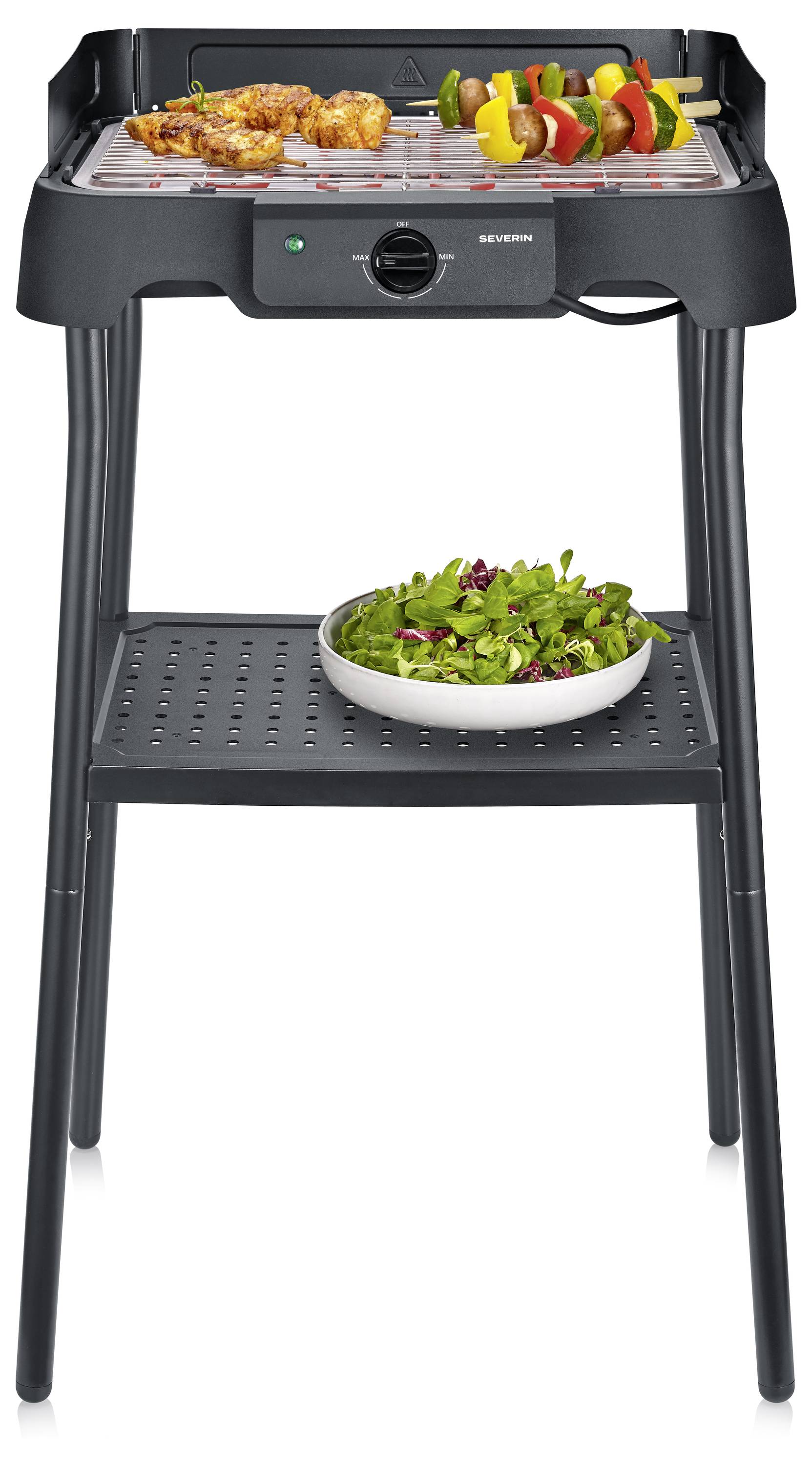 Schwarzer elektrischer Tischgrill auf einem Ständer, der Spieße grillt, mit einer Salatschüssel auf dem unteren Regal.