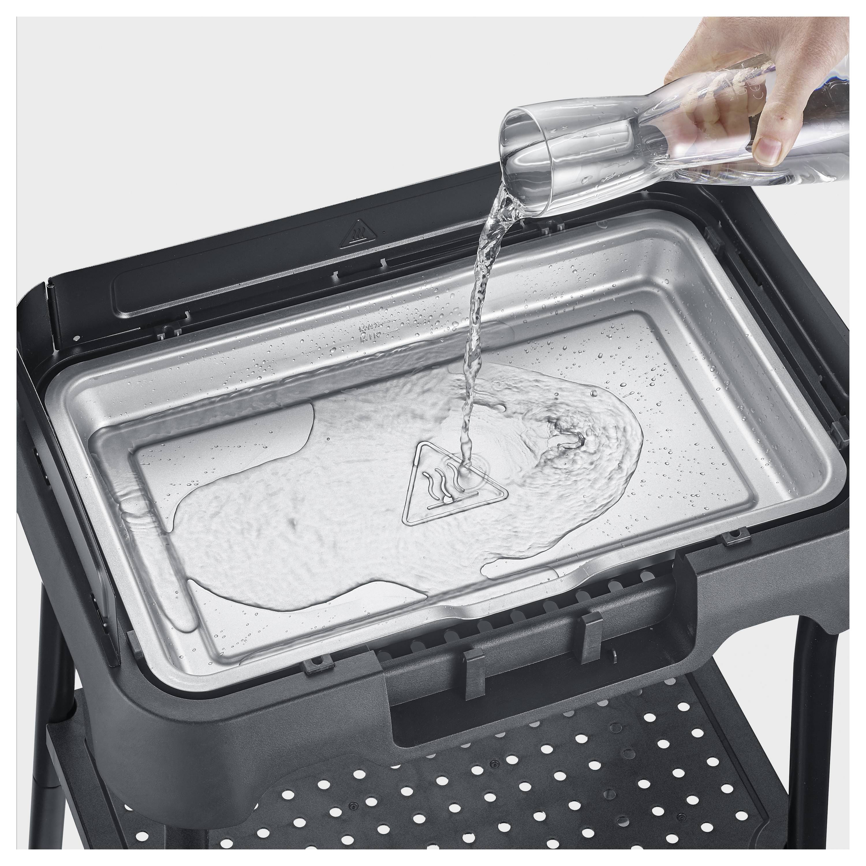 Eine Hand gießt Wasser aus einem Glas in eine abnehmbare Geräteablage und zeigt eine Füll- oder Reinigungsaktion.