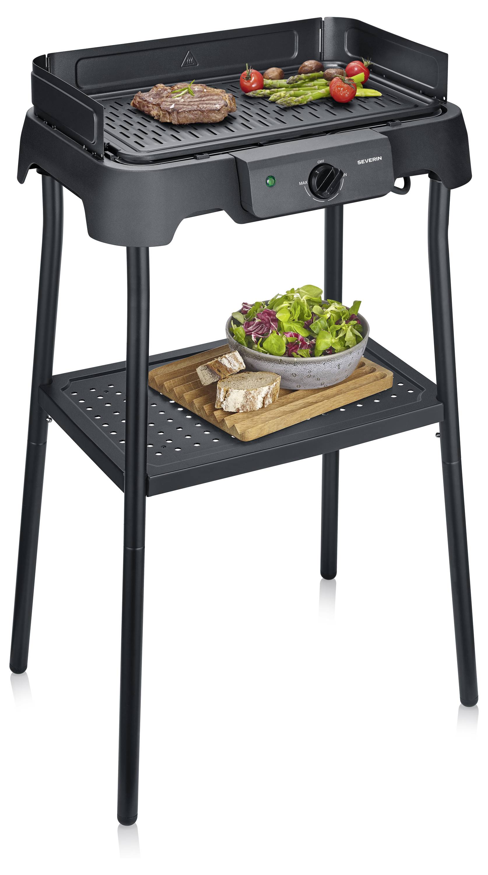 Elektrischer Tischgrill auf hohem Ständer, auf dem Steak, Spargel und Kirschtomaten gegrillt werden, mit unterem Regal, das Salat und Brot auf einem Schneidebrett hält.