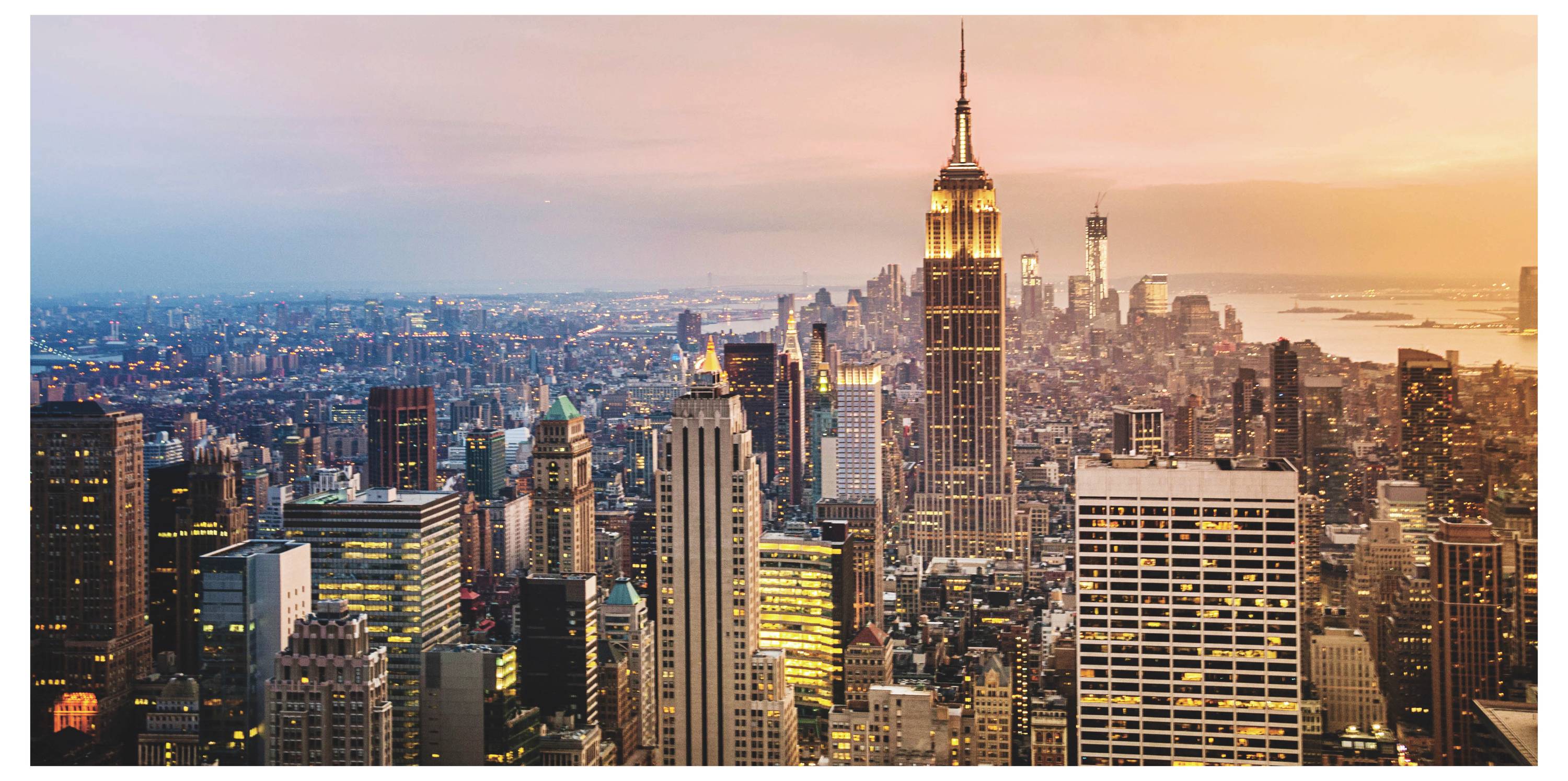 Skyline von New York City bei Sonnenuntergang, mit dem Empire State Building in der Mitte zwischen dicht gedrängten Hochhäusern und einem warmen orangefarbenen Himmel.