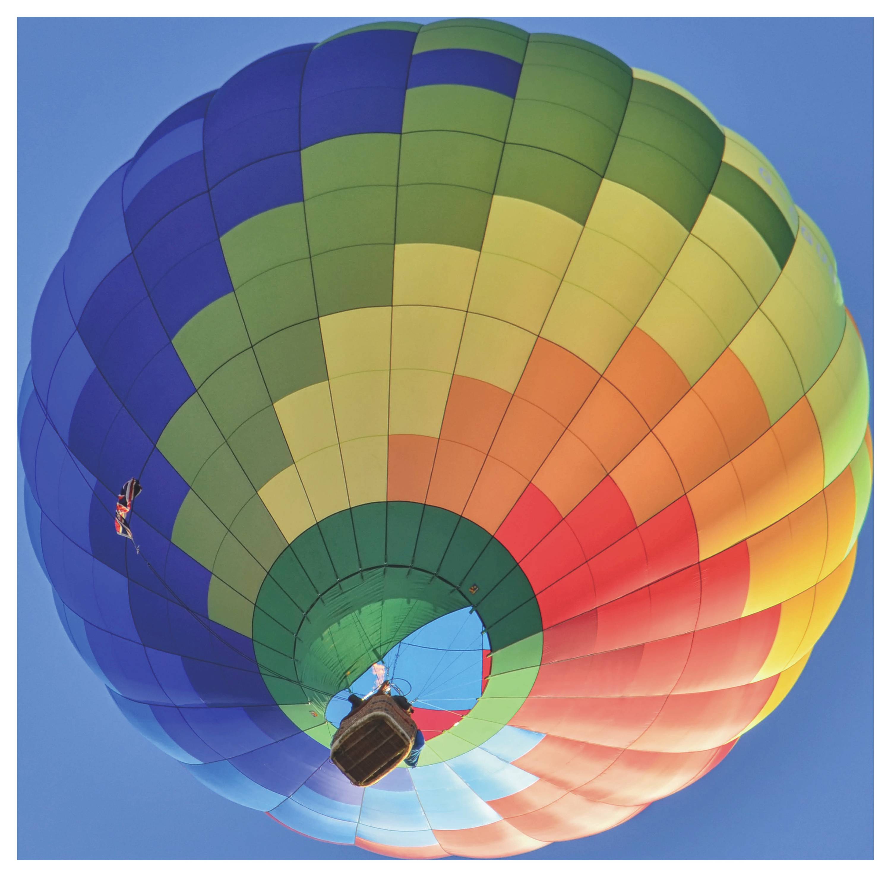 Bunter Heißluftballon von unten vor klarem blauem Himmel fotografiert, mit regenbogenfarbigem Baldachin und Korb.
