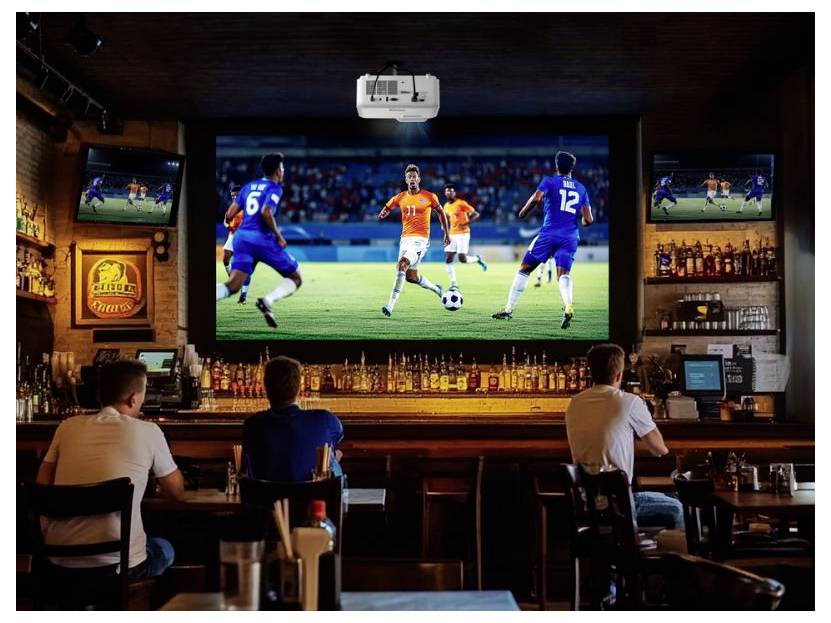 Kunden in einer Sportbar schauen sich auf einem großen Bildschirm ein Fußballspiel an, während kleinere Fernseher und die Bar hinter ihnen sichtbar sind.