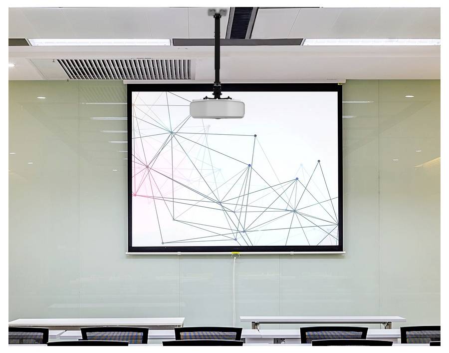 Meetingraum mit an der Decke montiertem Projektionsleinwand, die eine abstrakte geometrische Liniengrafik über leeren Schreibtischen und Stühlen anzeigt.