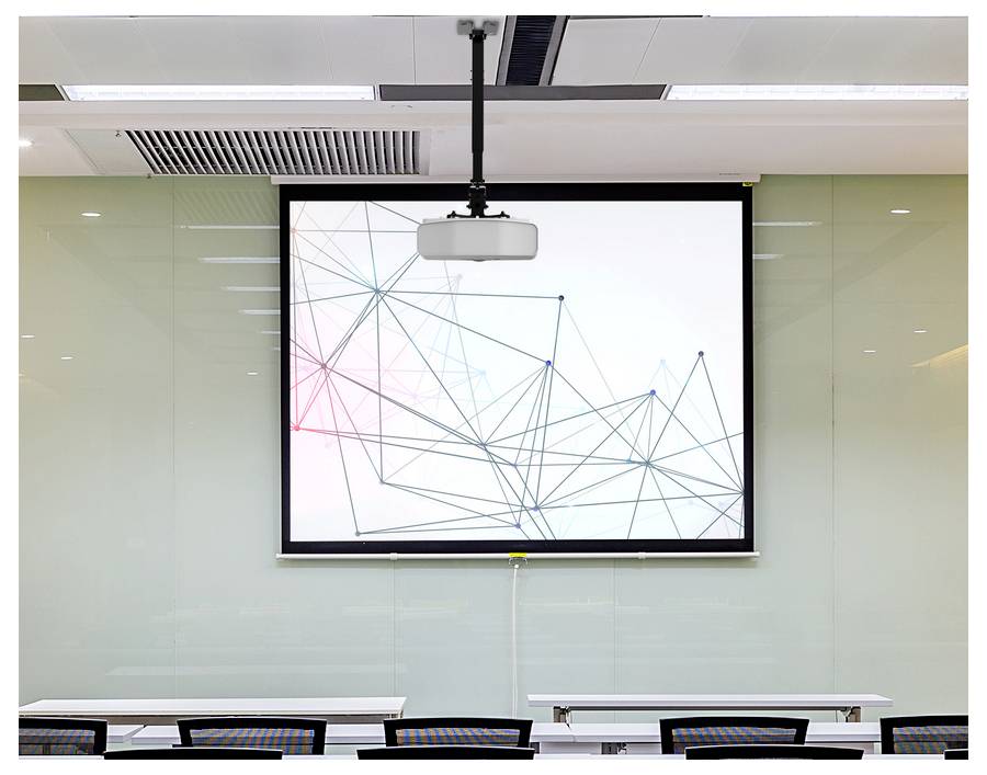 Klassenzimmer mit an der Decke montiertem Projektor und ausziehbarem Bildschirm, auf dem ein abstraktes Netzwerk-ähnliches Diagramm angezeigt wird; leere Schreibtische davor.