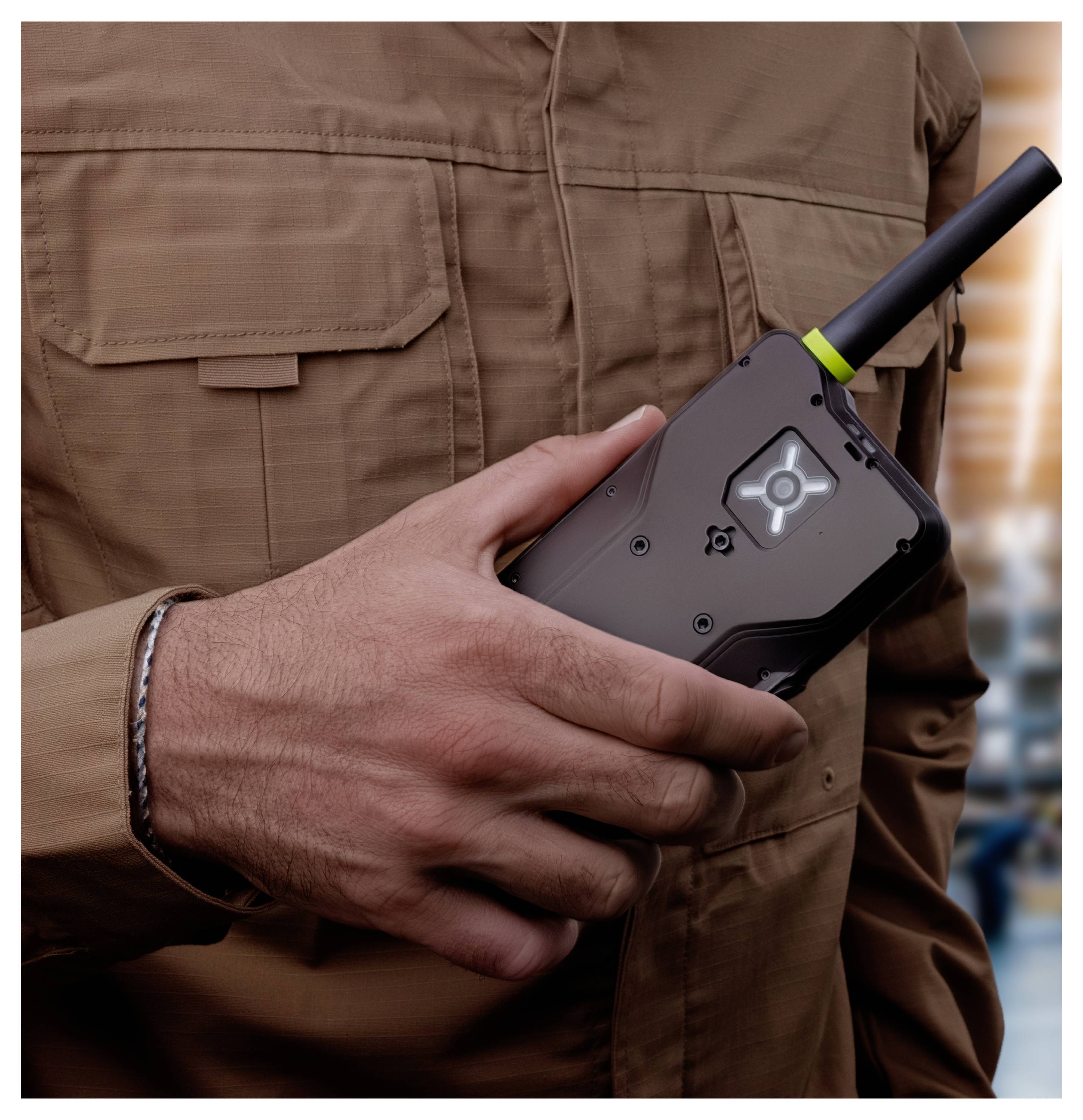 Person in a brown jacket holding a black handheld two-way radio with antenna and illuminated screen.Personen in einer braunen Jacke, die ein schwarzes tragbares Funkgerät mit Antenne und leuchtendem Bildschirm halten.