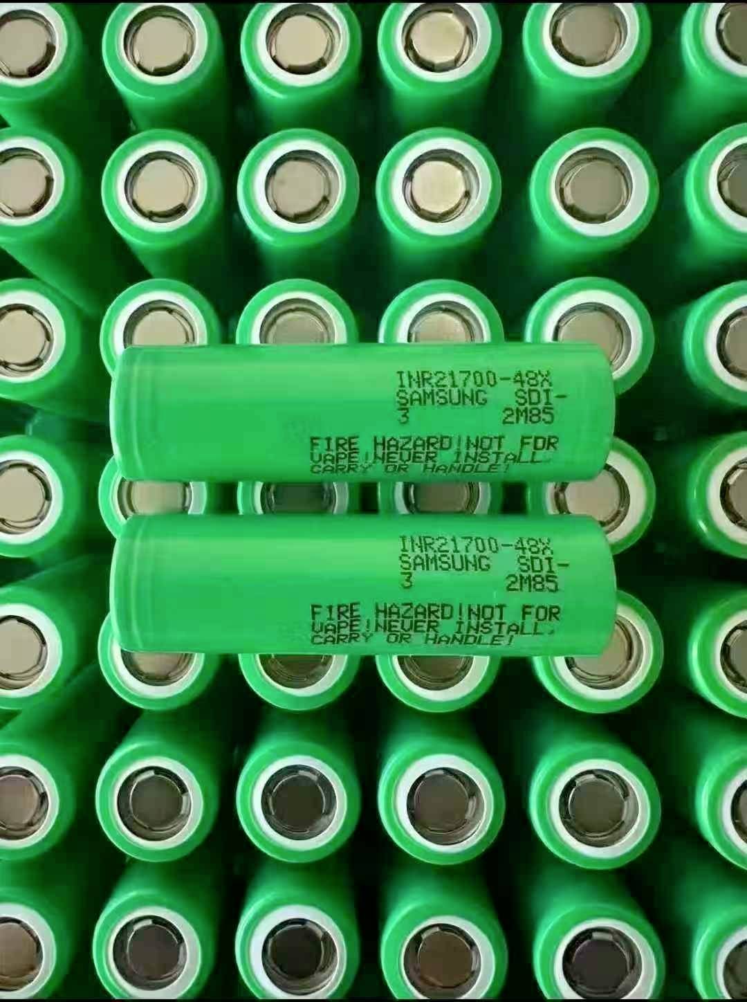 Nahaufnahme von grünen wiederaufladbaren Samsung INR21700-48G-Batteriezellen, die in Reihen angeordnet sind, mit zwei Batterien, die horizontal über vielen aufrecht stehenden Zellen liegen.