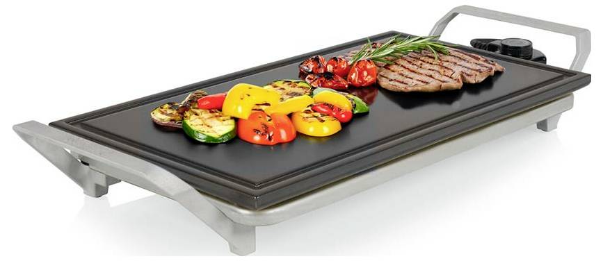 Elektrischer Tischgrill zum Kochen von Steak, Garnelen und in Scheiben geschnittenem Gemüse auf einer schwarzen antihaftbeschichteten Grillplatte.