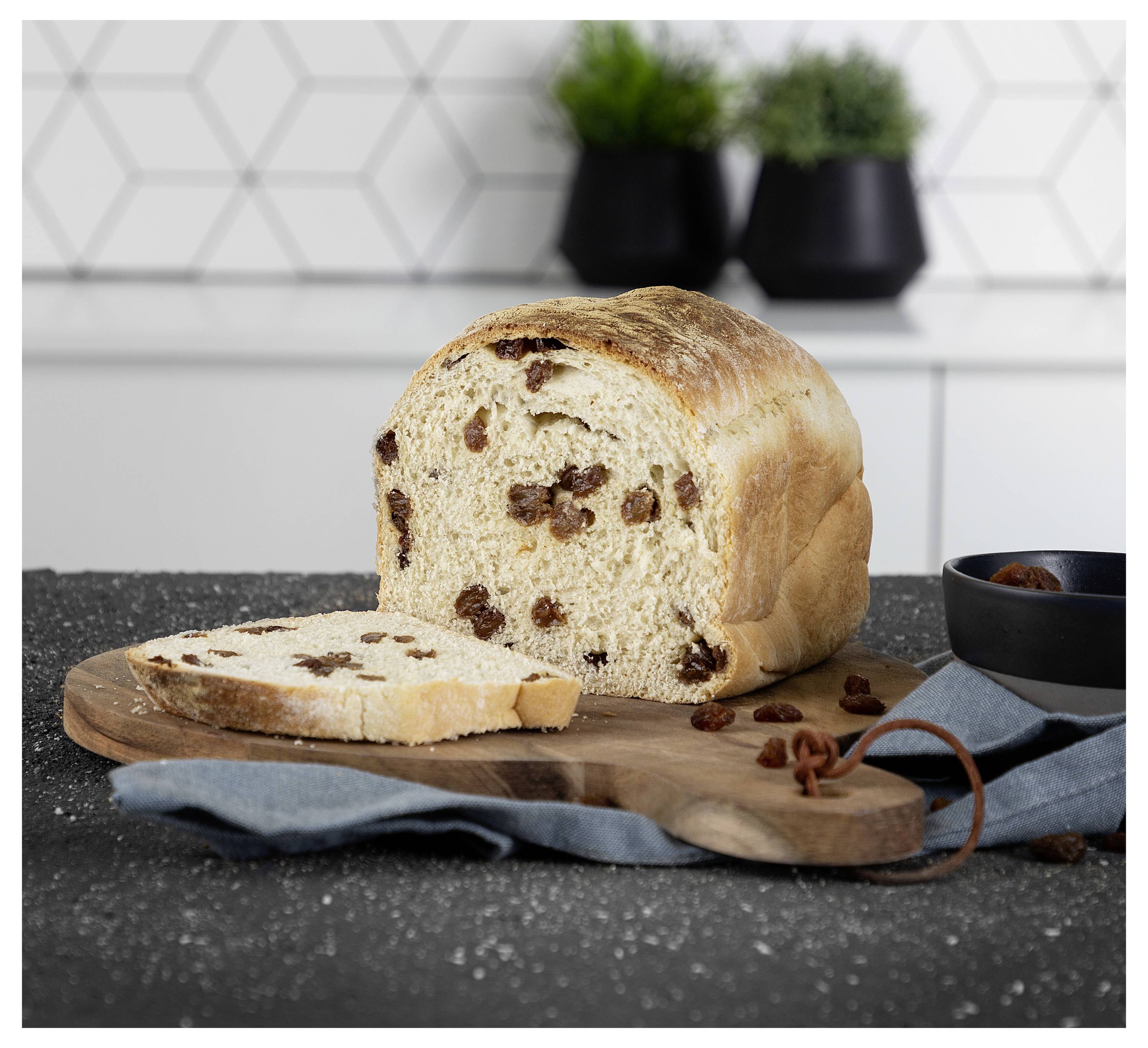 Ein Laib Rossinenbrot auf einem Schneidebrett, mit einer abgeschnittenen Scheibe, die vorne auf einer Küchenarbeitsplatte liegt.