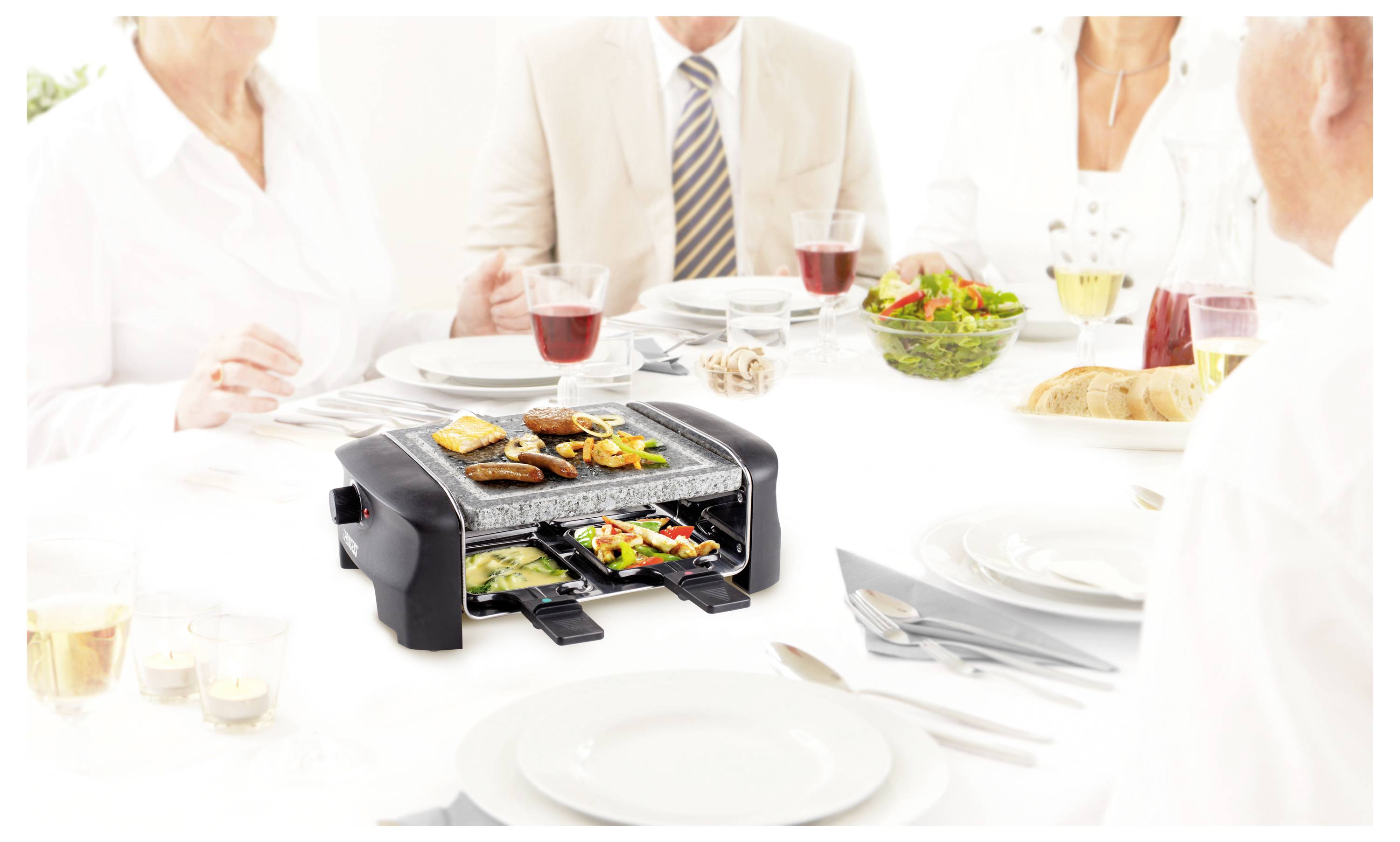 Menschen versammelten sich um einen Esstisch herum und benutzten einen Tischgrill mit verschiedenen Lebensmitteln, was auf ein gemeinsames Essen oder ein Raclette-ähnliches Abendessen hindeutet.