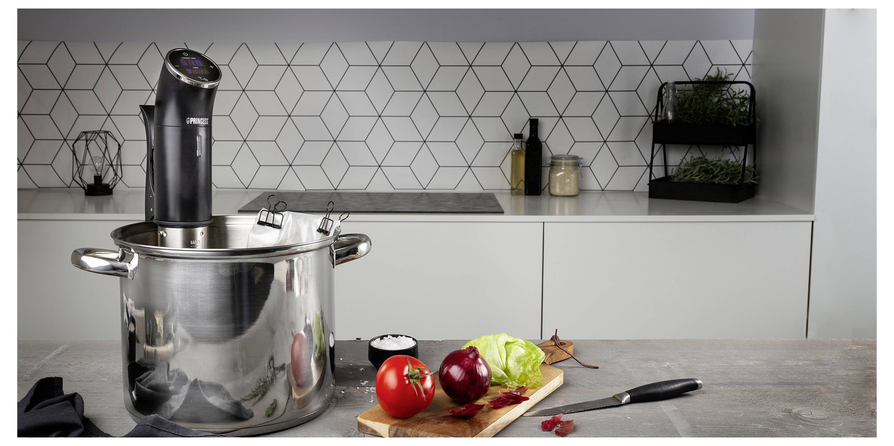 Moderne Küchentheke mit einem großen Edelstahltopf, einem Stabmixer und gehacktem Gemüse auf einem Schneidebrett, bereit zum Kochen.