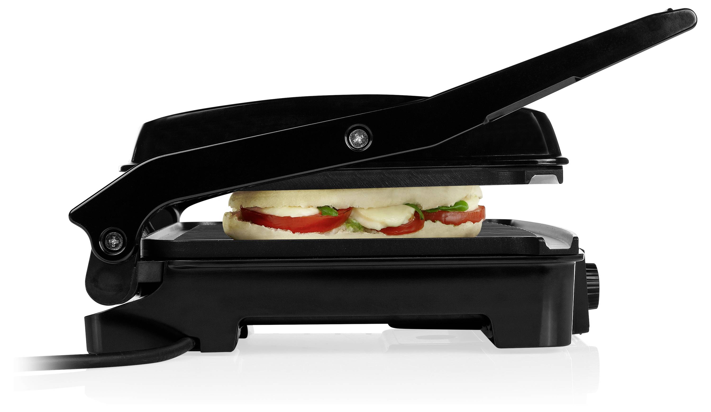 Geschlossene schwarze Sandwichpresse, die ein Sandwich mit sichtbarer Tomaten- und Käsefüllung auf weißem Hintergrund grillt.