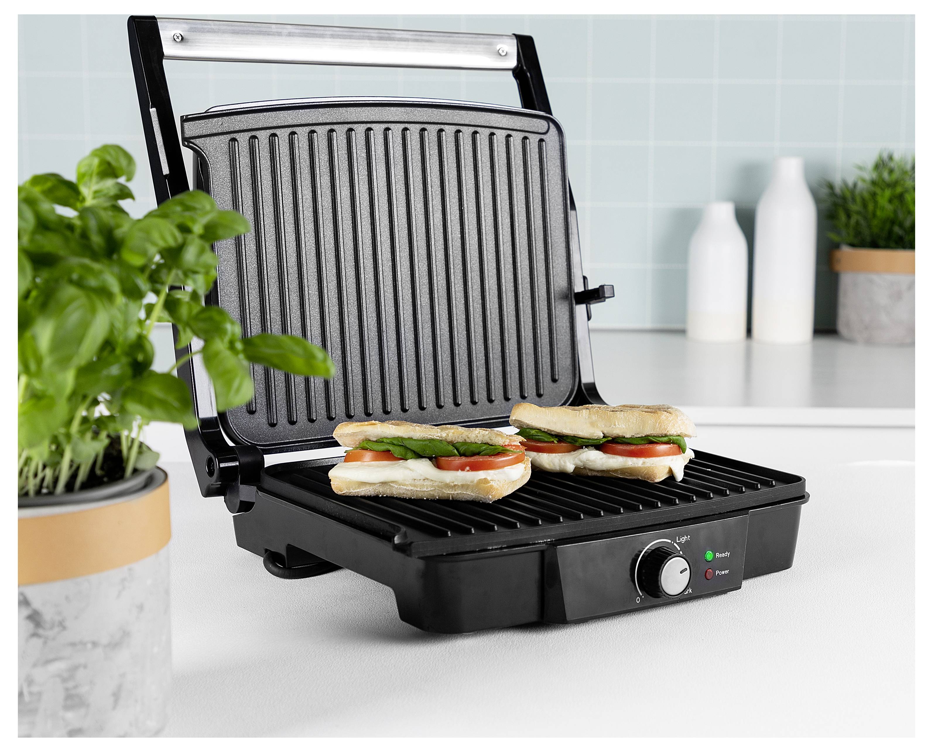 Offener elektrischer Kontaktgrill mit drei Sandwich-Hälften auf den Grillrosten in einer Küchenumgebung.