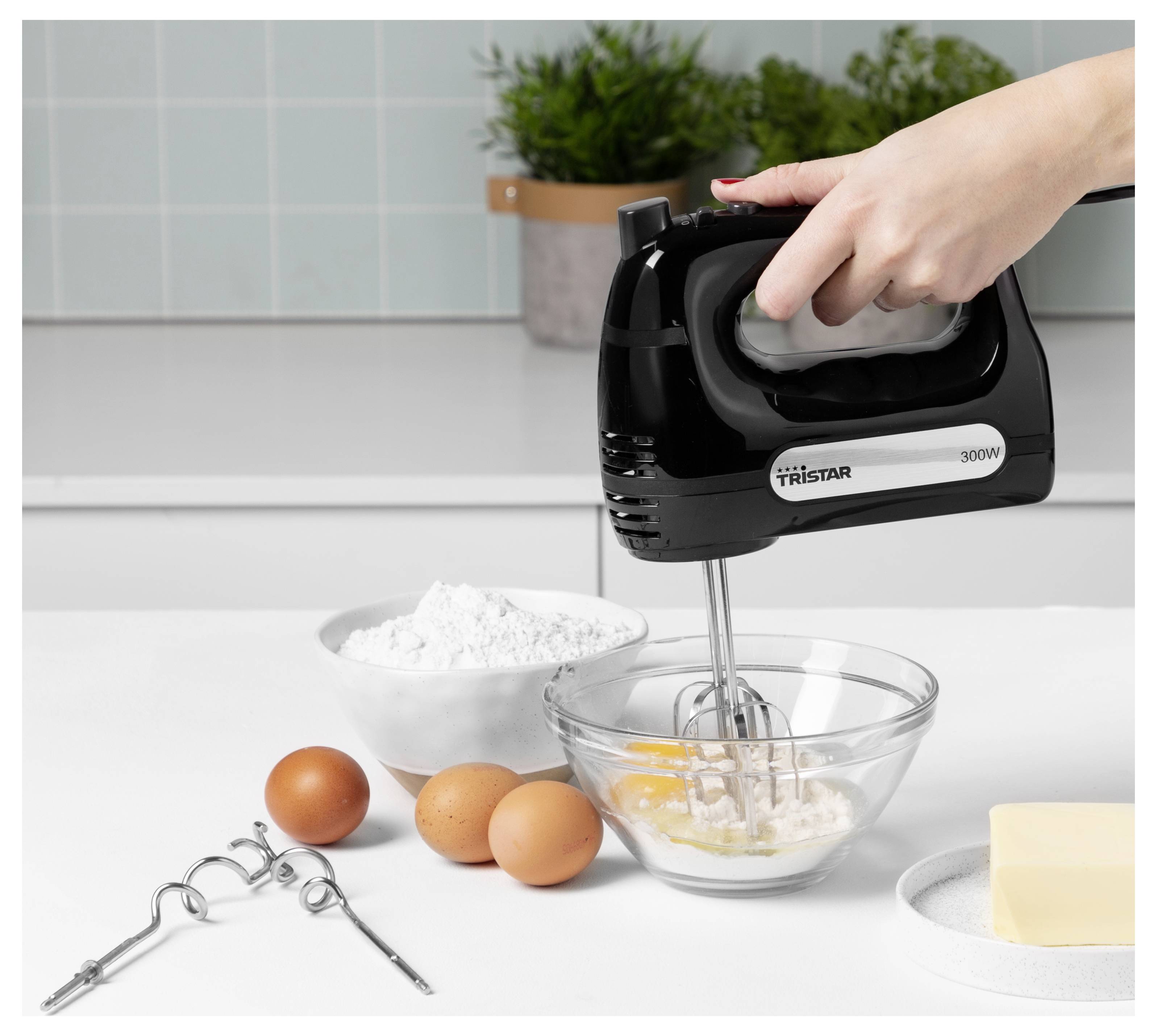 Handmixer schlägt Zutaten in einer Glasschüssel auf einer Küchentheke auf, mit Eiern, Mehl, Rührbesenm und Butter in der Nähe.