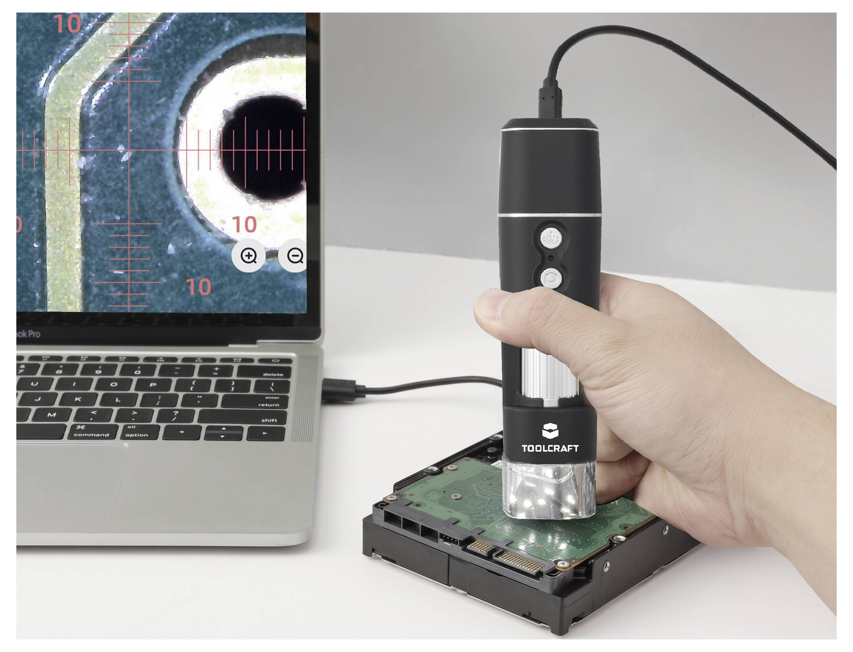 Tragbares digitales Mikroskop inspiziert eine Festplattenleiterplatte neben einem Laptop, der eine vergrößerte Ansicht anzeigt.