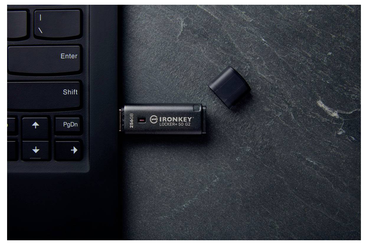 USB-Sicherheitsschlüssel, der neben der Tastatur in einen Laptop gesteckt ist, mit seiner Kappe daneben auf einem dunklen Schreibtisch.