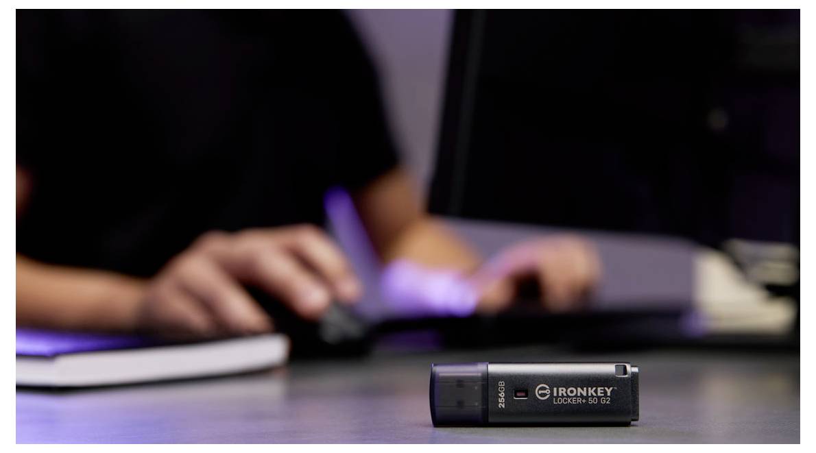 Nahaufnahme eines IronKey USB-Sticks auf einem Schreibtisch, mit einer unscharfen Person, die im Hintergrund tippt.