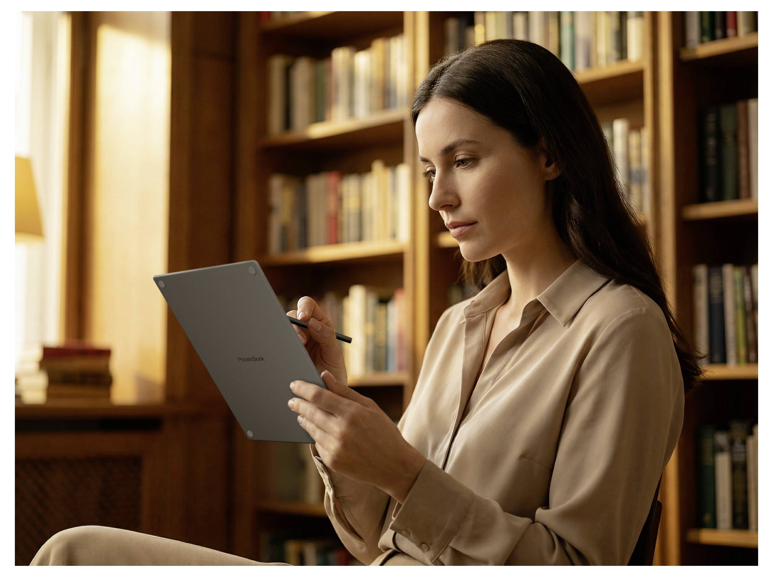 Frau sitzt in einer Bibliothek und schreibt auf einem Tablet mit einem Stift, während sie liest, mit Bücherregalen im Hintergrund.