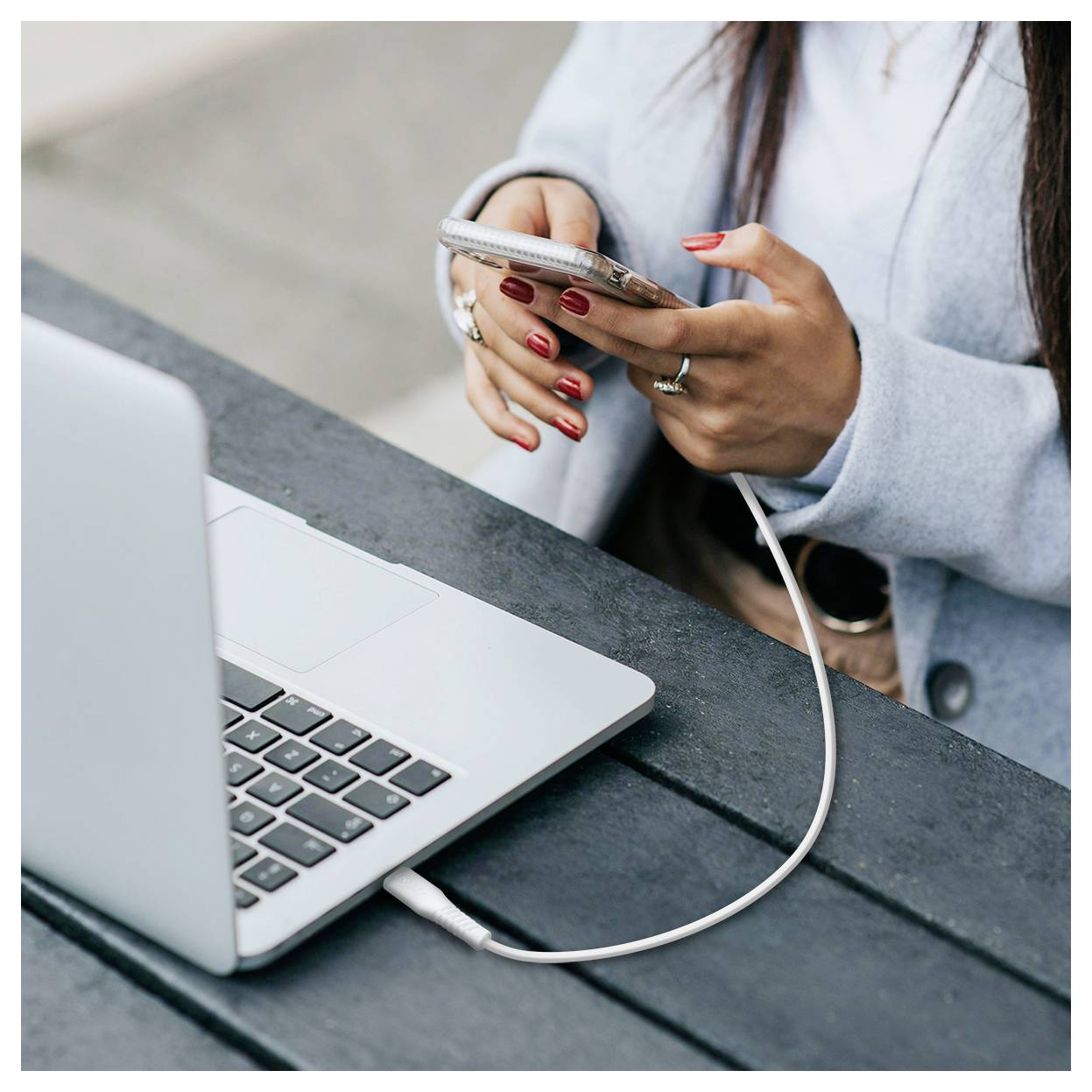 Person charging a smartphone with a cable next to an open laptop on a table.