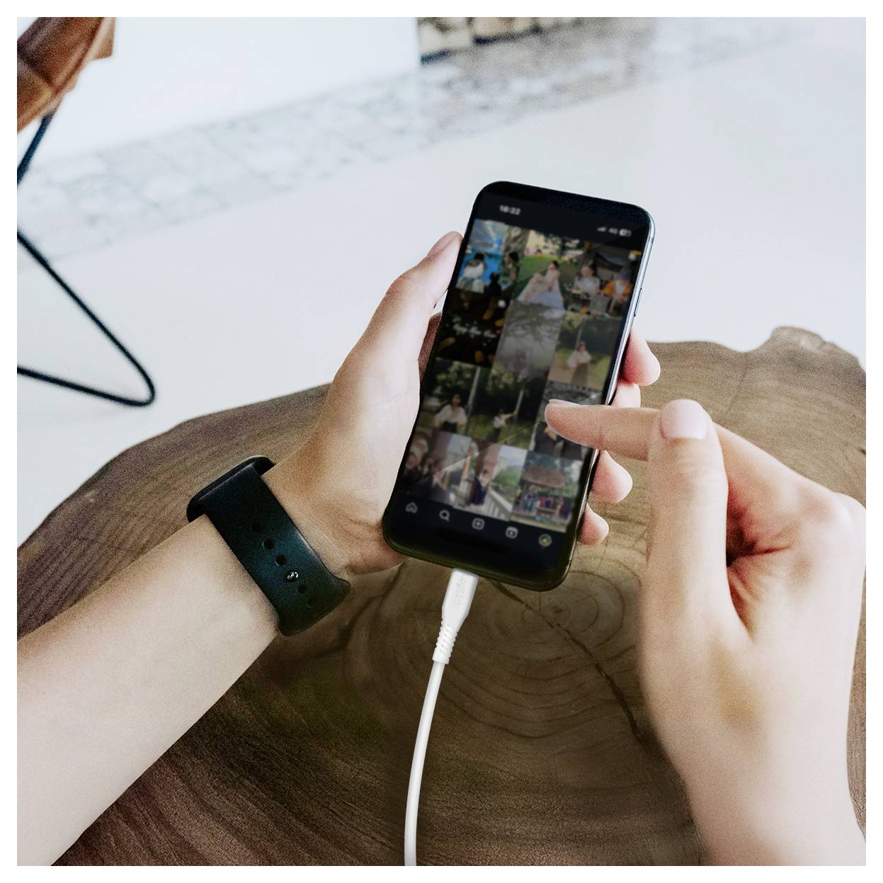 Person blättert durch eine Fotogalerie auf einem Smartphone, während sie es mit beiden Händen an einem Tisch hält, mit angeschlossenem Ladekabel.
