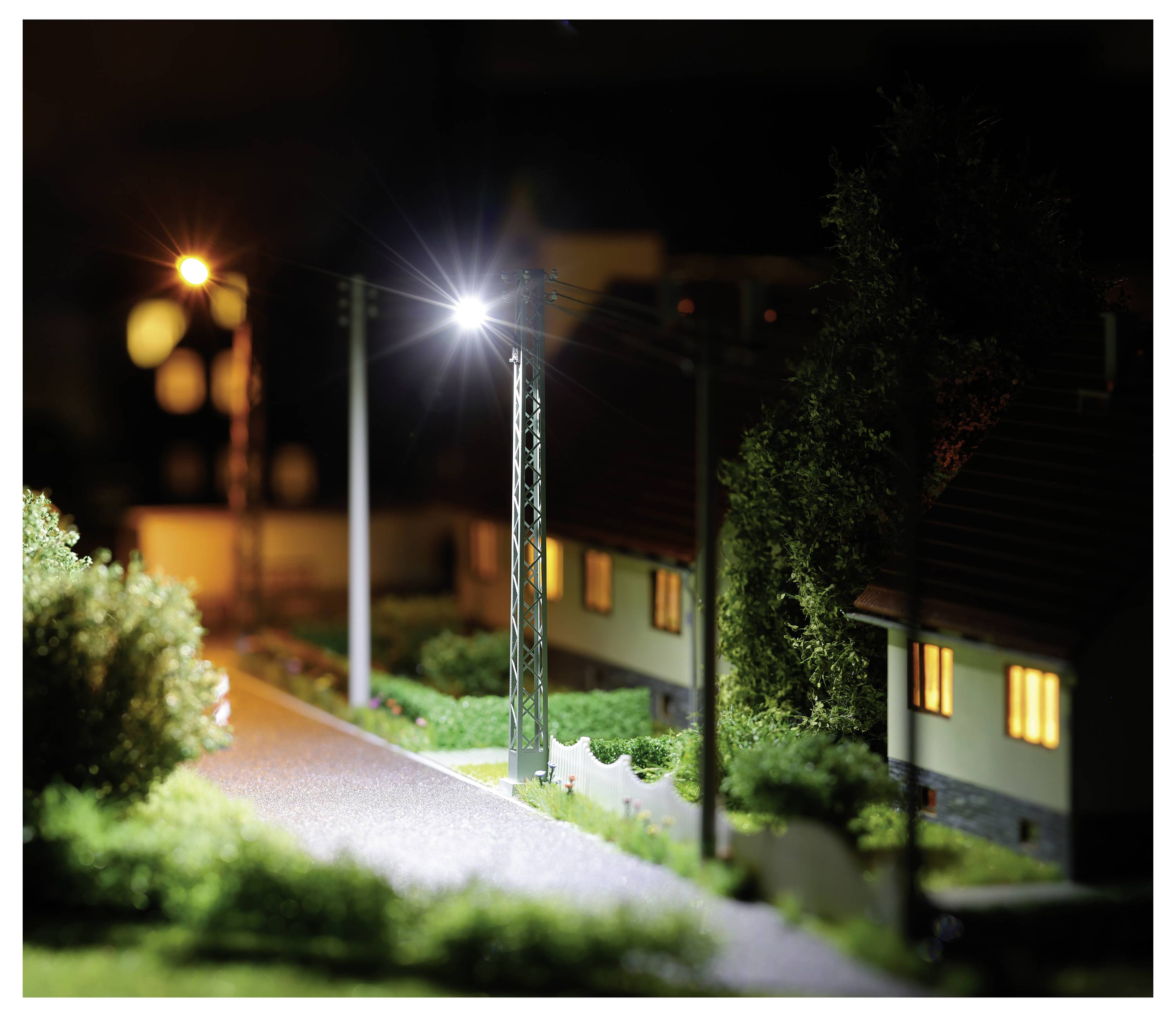 Nächtliches Miniaturmodell einer Wohnstraße mit beleuchteten Straßenlaternen, leuchtenden Hausfenstern und Bäumen entlang einer Straße.