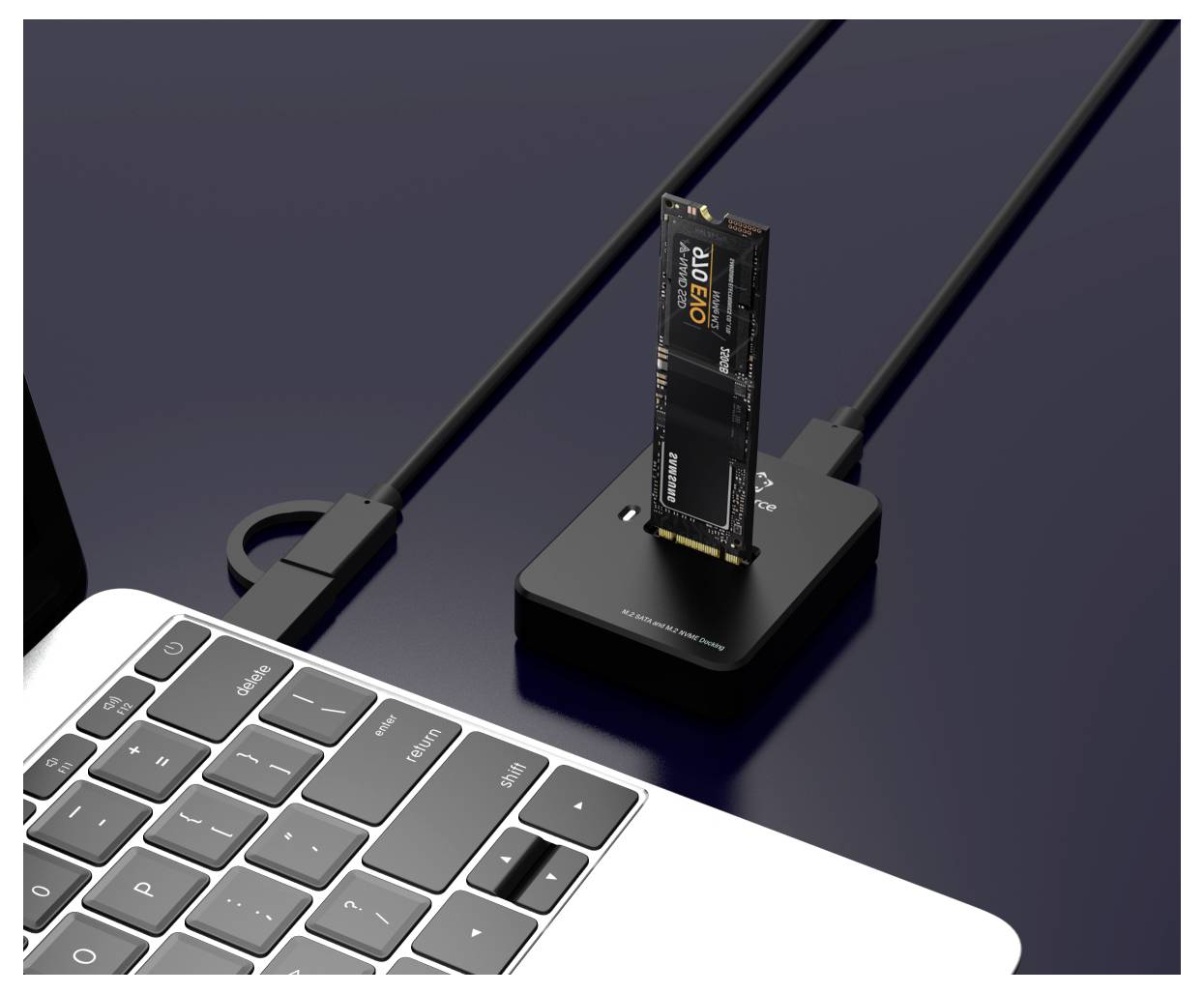Kleine externe SSD, die in ein kompaktes schwarzes Dock neben einer Laptop-Tastatur angeschlossen ist, mit Kabeln, die auf einem dunklen Schreibtisch verbunden sind.