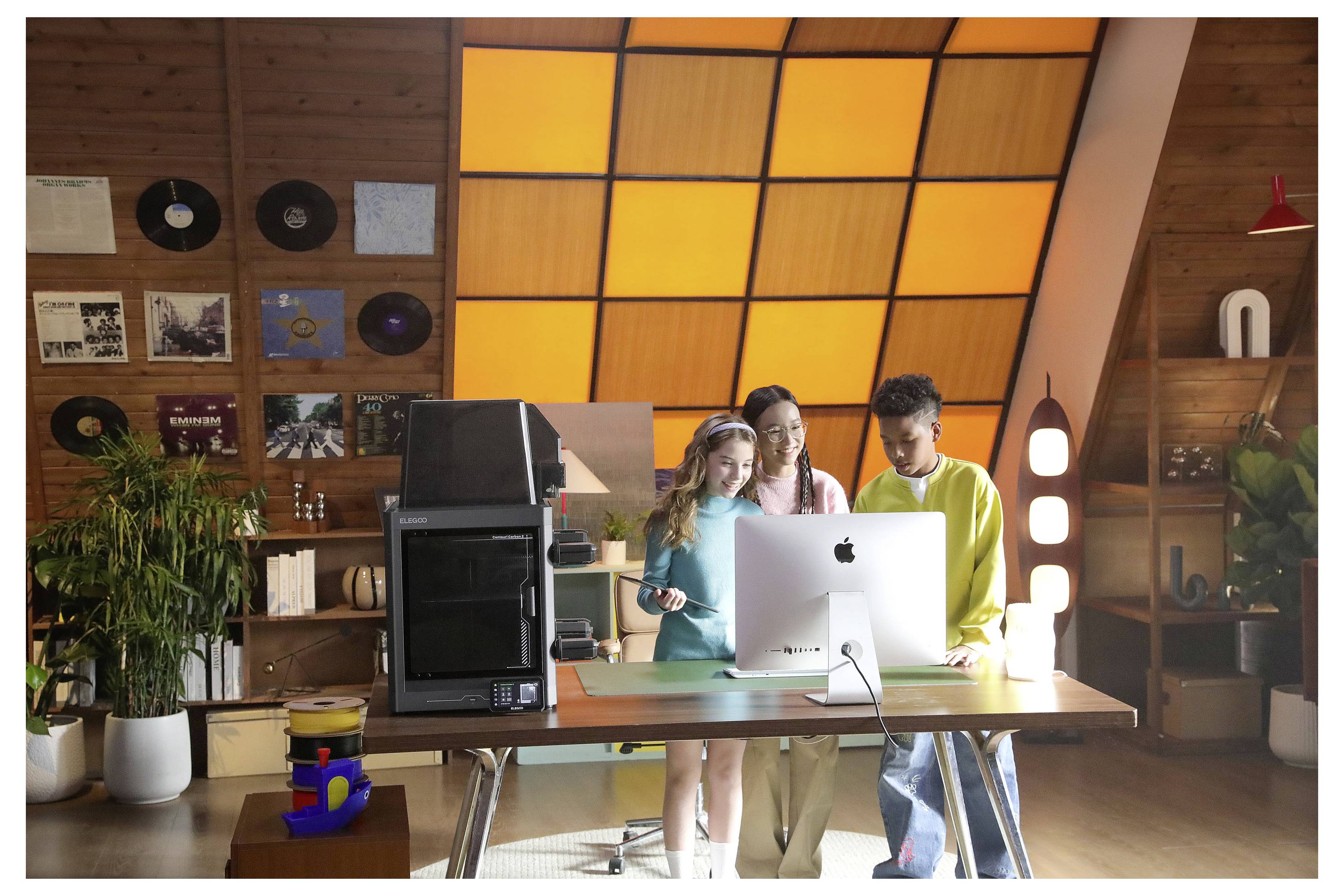 Drei Personen arbeiten zusammen an einem iMac in einem warmen, holzvertäfelten Büro mit einer leuchtenden orange gefärbten Fensterfront.