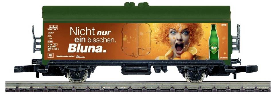 Ein grüner Güterwagen mit einer orangefarbenen Bluna-Werbung, auf der eine schreiende Frau und der Slogan „Nicht nur ein bisschen. Bluna.