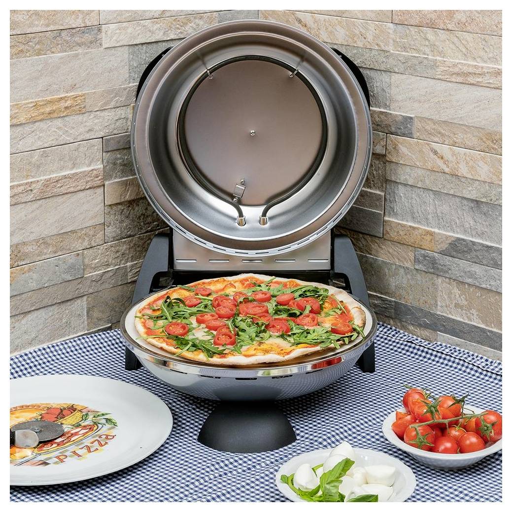 Outdoor-Arbeitsplatte Pizzaofen mit einer Pizza im Inneren beim Backen, umgeben von Tellern und Schüsseln mit frischen Belägen auf einer karierten Tischdecke.