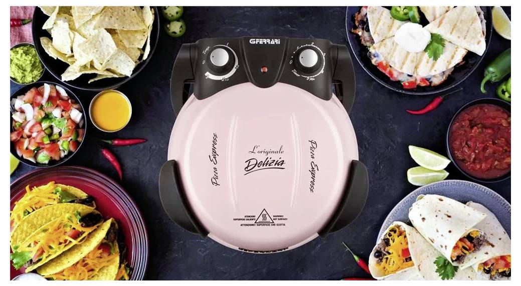 Rosa G3 Ferrari Elektro-Pizzaofen in der Mitte eines Tisches, umgeben von vorbereiteten Zutaten sowie servierten Tacos und Chips.