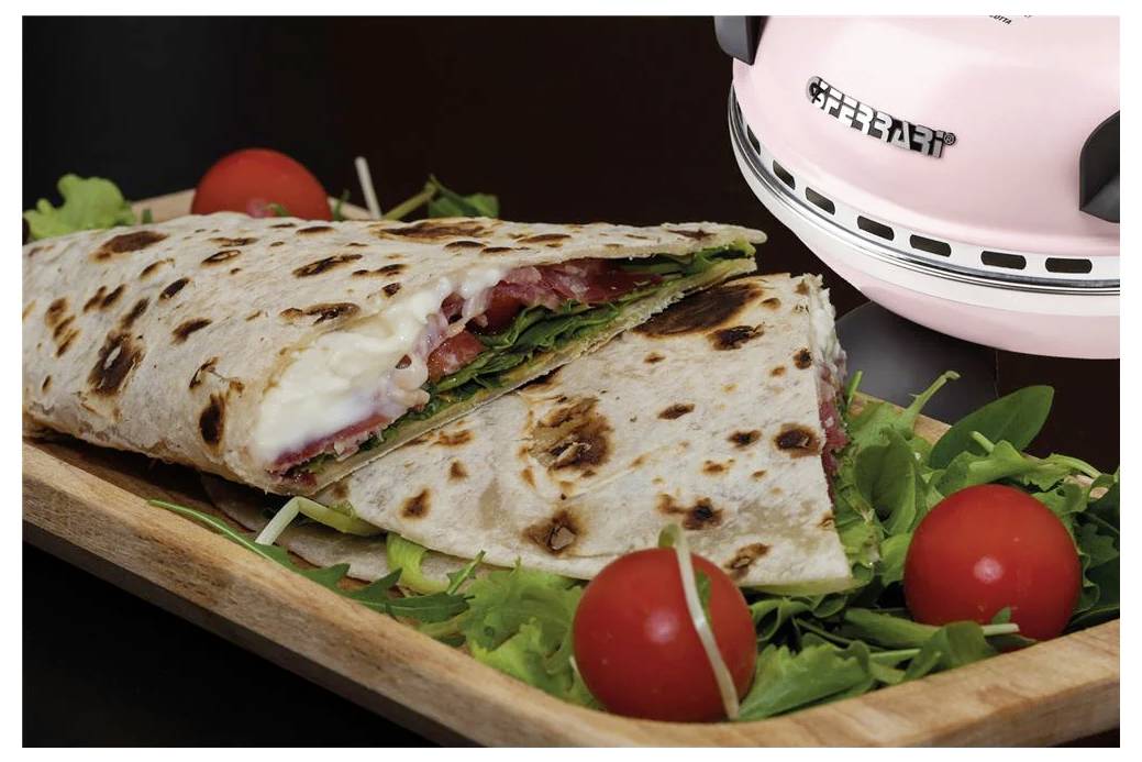 Gegrilltes gefaltetes Fladenbrot-Sandwich auf einem Holzbrett mit Kirschtomaten und Grünzeug, neben einer rosafarbenen Sandwichpresse.