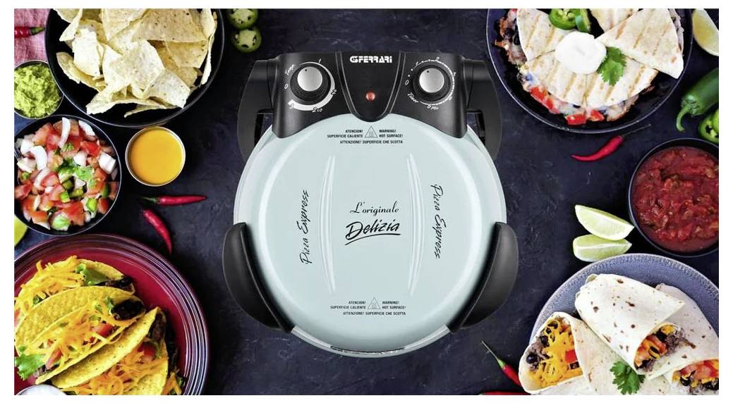 Draufsicht eines mintgrünen G3Ferrari-Pizzamakers, umgeben von Tortilla-Chips, Tacos, Salsa, Guacamole und Limettenspalten auf einem dunklen Tisch.