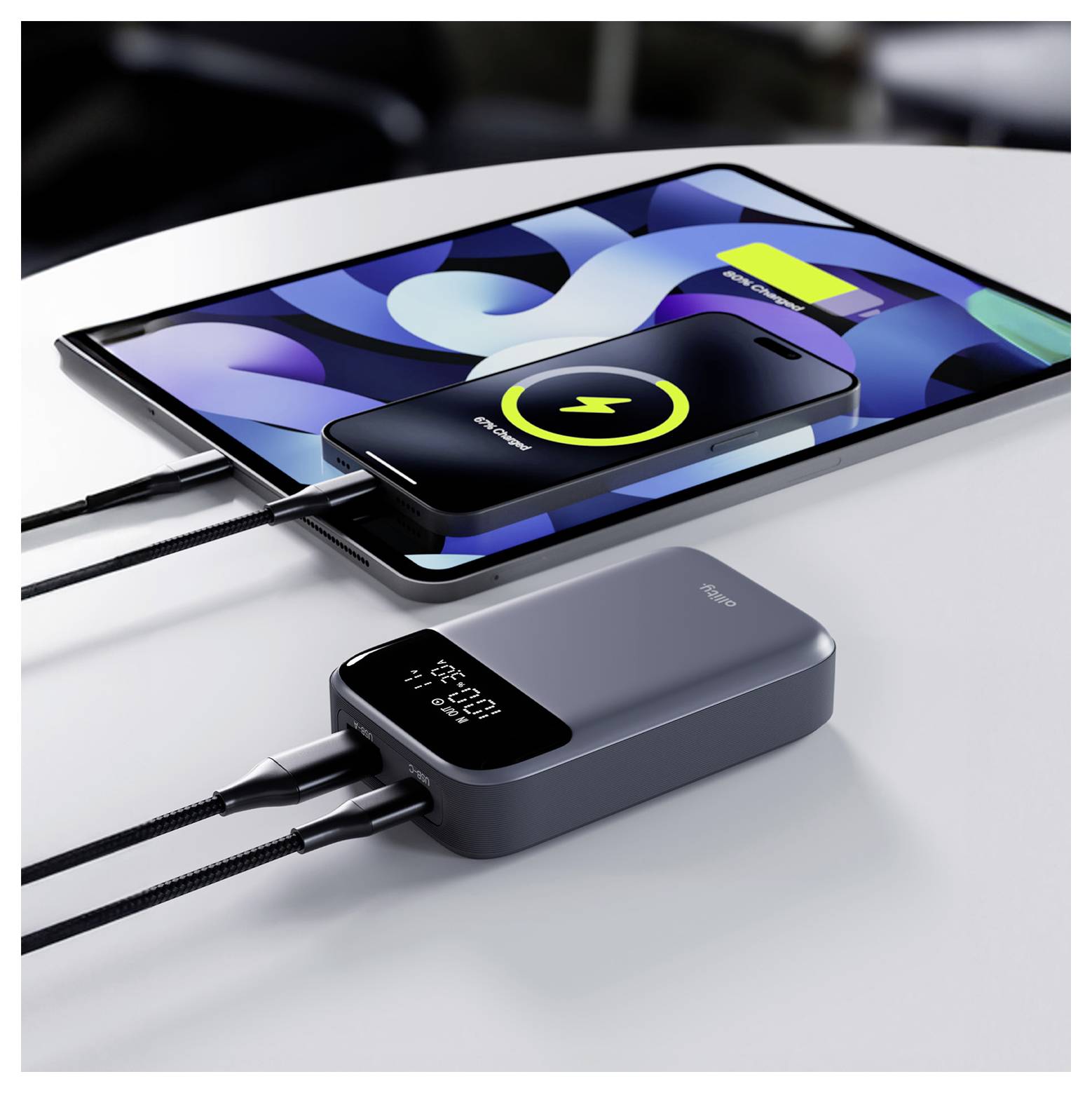 Kabelloses Ladesystem mit einem Smartphone, das auf einem Tablet aufgeladen wird, verbunden durch Kabel mit einer tragbaren Powerbank auf einer Tischplatte.