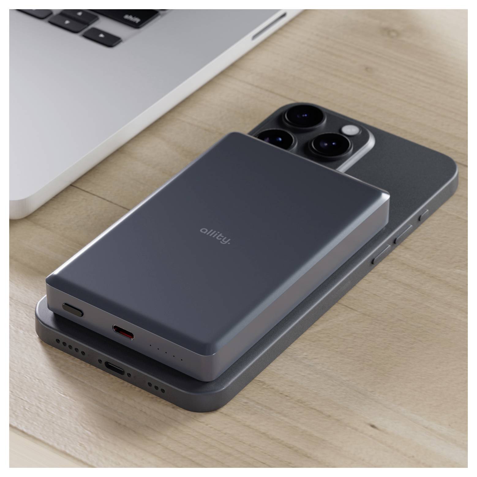 Zwei übereinander gestapelte Smartphones auf einem Schreibtisch, wobei ein dunkles Anker-Akku-Pack das obere Telefon neben einem Laptop auflädt.
