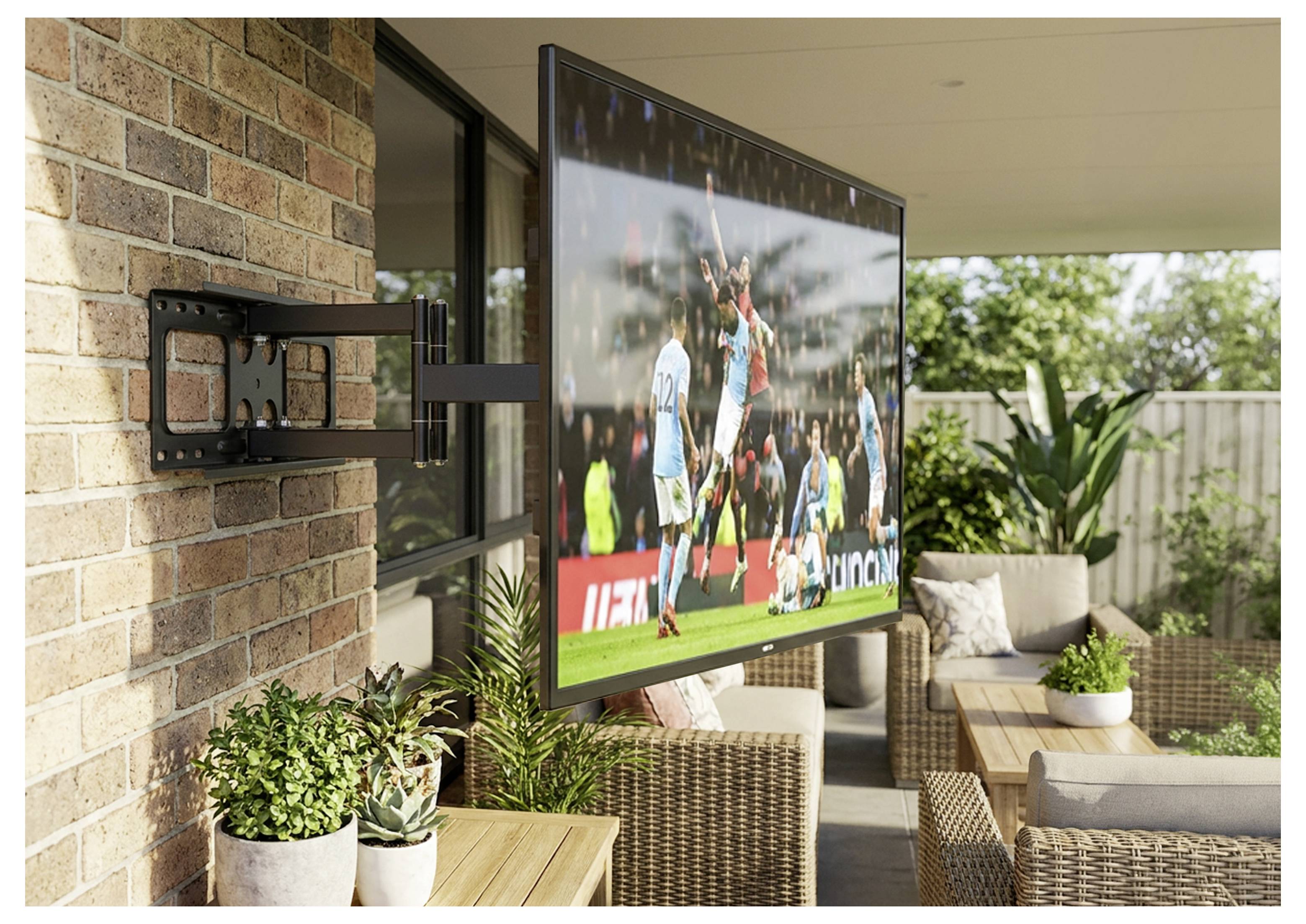 Flachbildfernseher an einer Backsteinmauer auf einer Terrasse montiert, zeigt ein Fußballspiel in einem Außensitzbereich mit Korbmöbeln und Pflanzen.