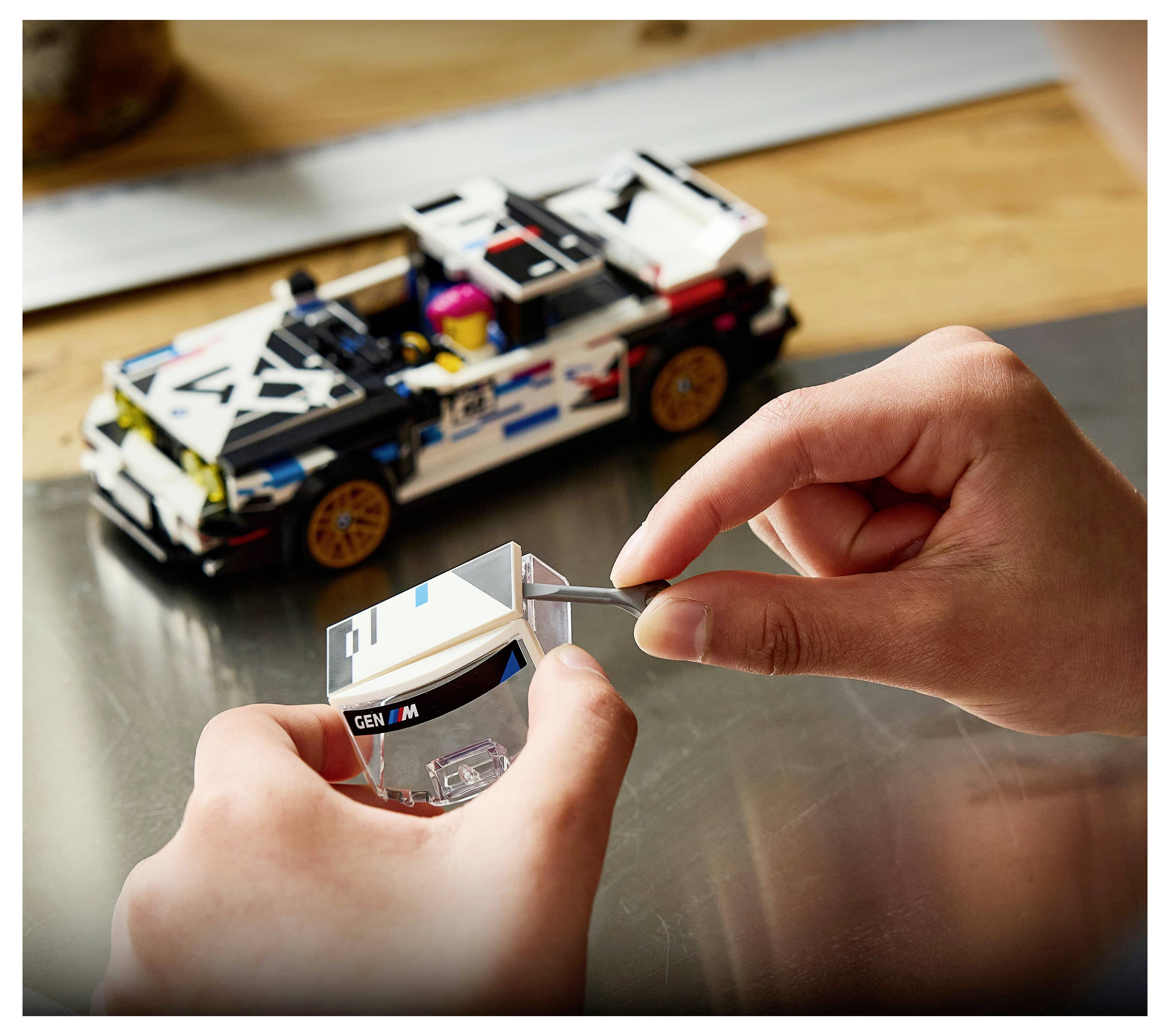 Kind, das ein weiß-schwarzes Spielzeugrennwagen mit einem transparenten Teil zusammenbaut, mit dem teilweise gebauten Auto auf einem Tisch im Hintergrund.