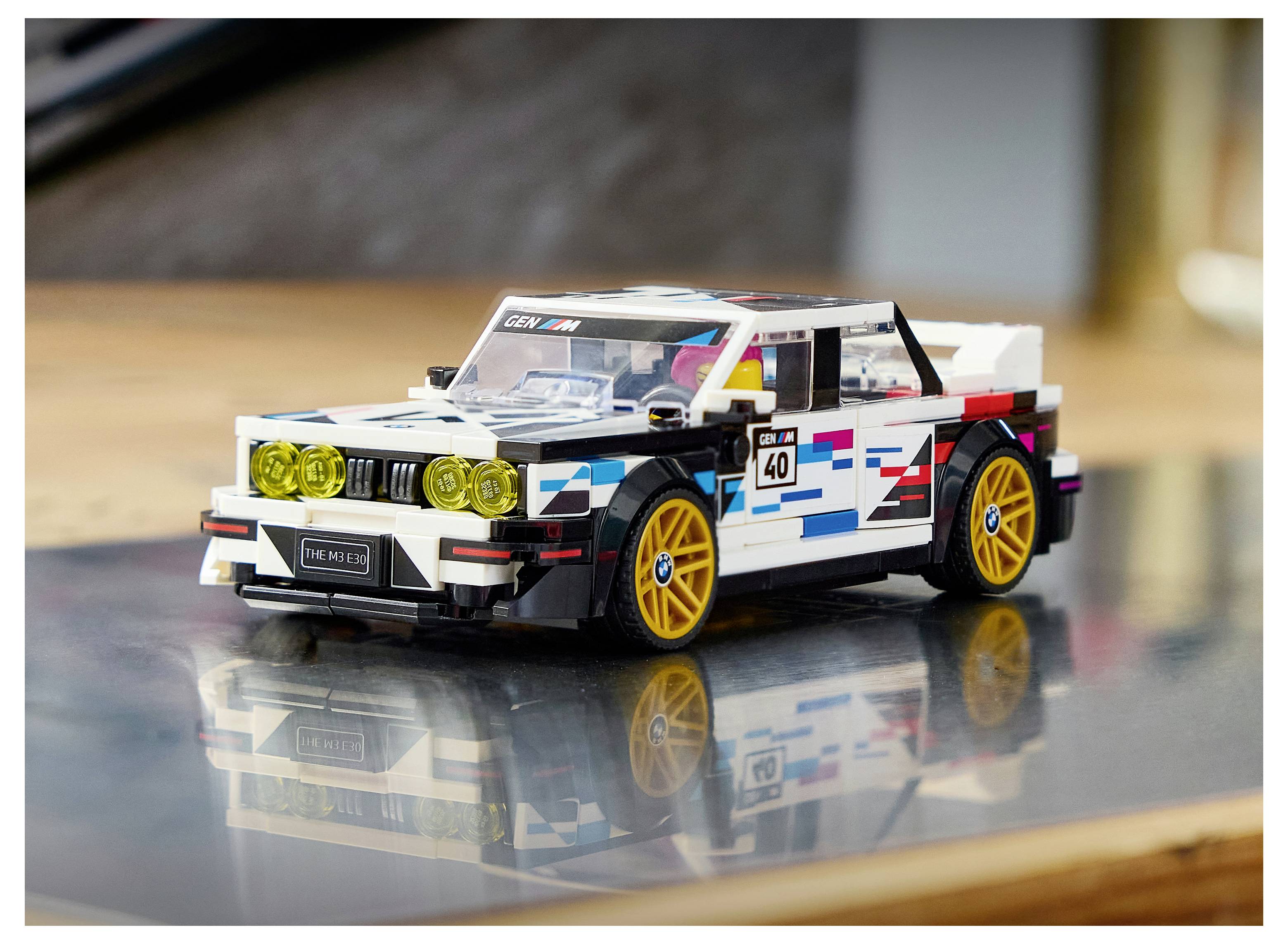 Weißes LEGO-Rennwagen mit gelben Rädern auf einer reflektierenden Oberfläche, seitlich von vorne in Innenräumen dargestellt.