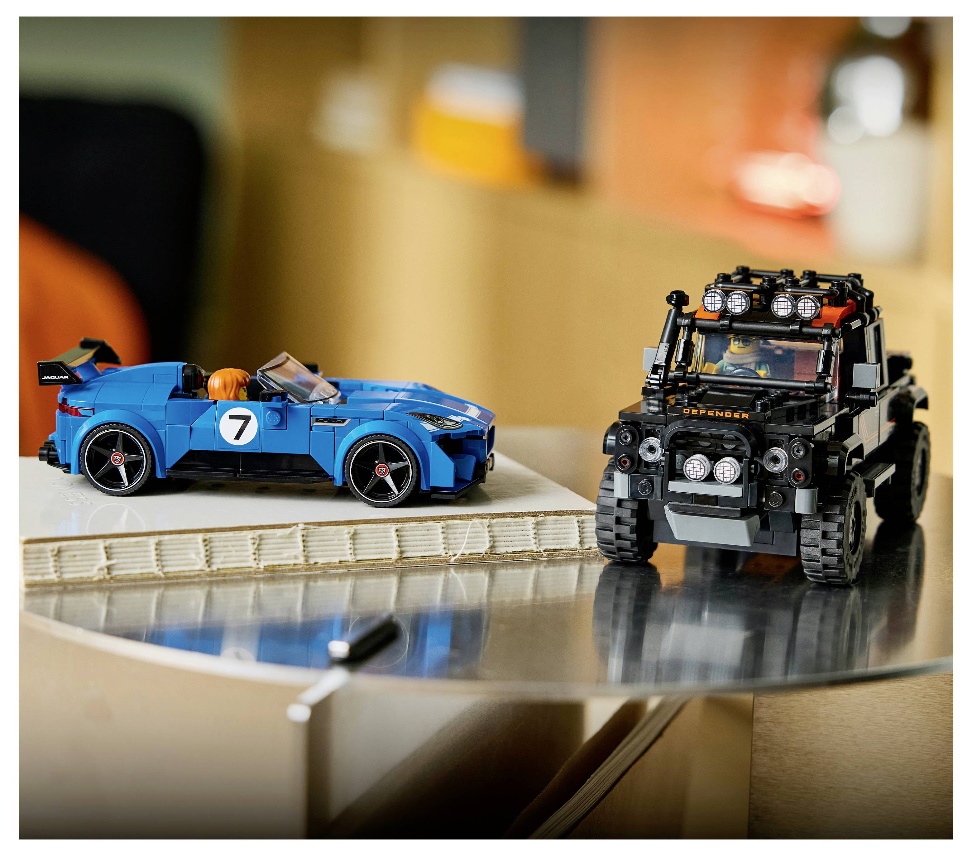 Ein blaues Rennwagen-Spielzeug und ein schwarzes Gelande-SUV-Spielzeug werden auf einem Tisch ausgestellt, wobei das SUV im Vordergrund und das Auto dahinter positioniert sind.
