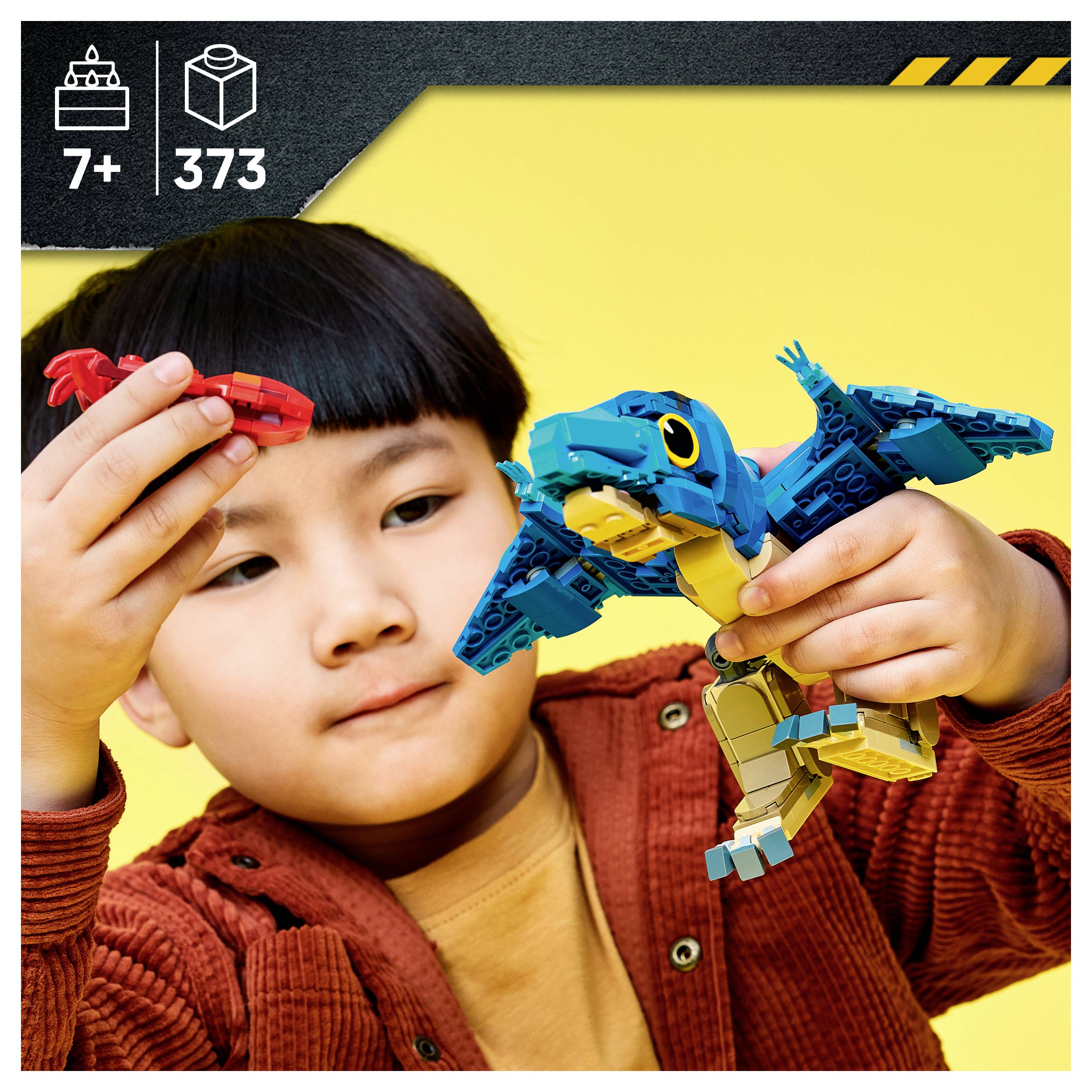 Kind spielt mit LEGO-ähnlichem Vogelmodell; Schachtelkunstwerk zeigt Altersangabe 7+ und 373 Teile auf gelbem Hintergrund.