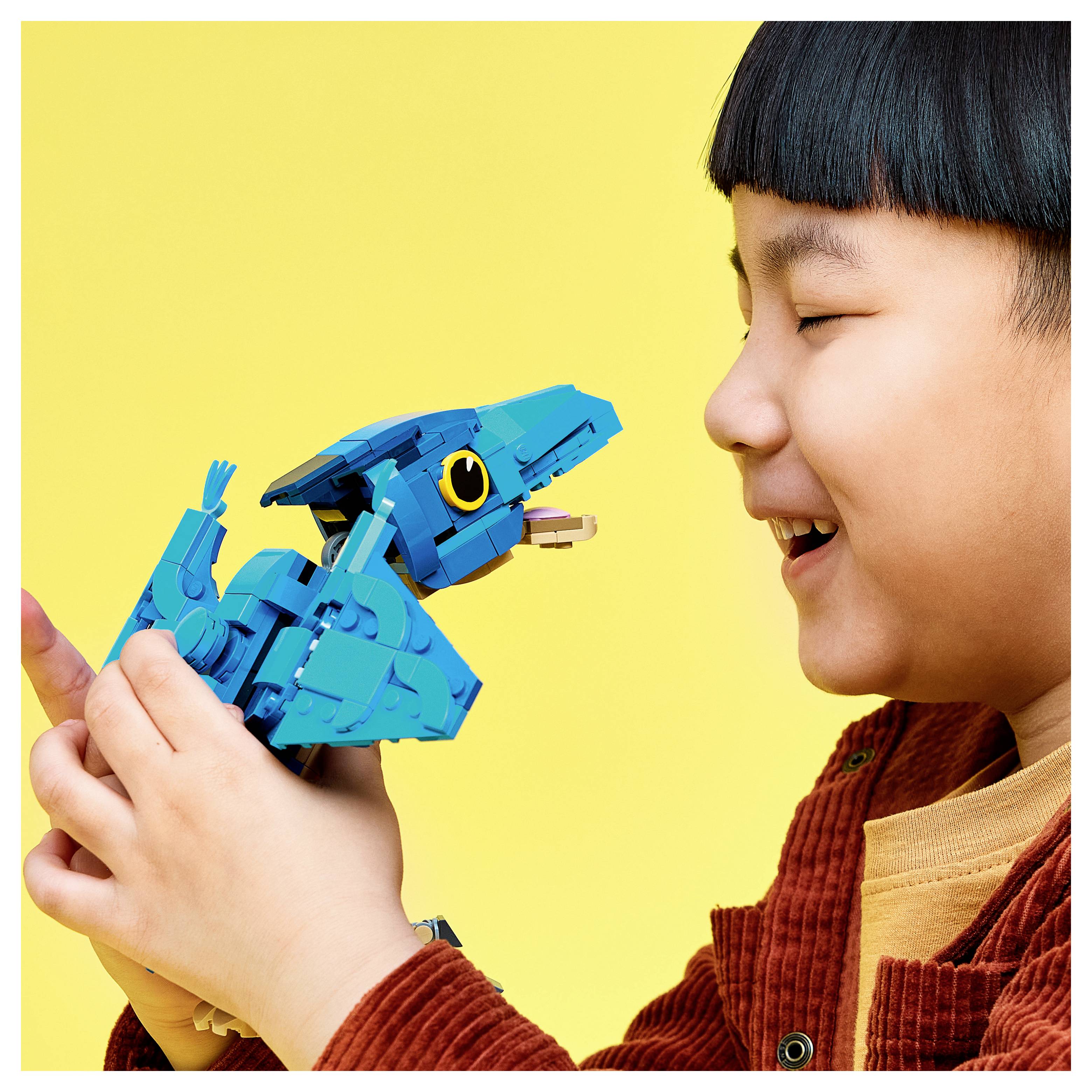 Ein lächelndes Kind schaut auf einen blauen Spiel-Dinosaurier vor einem gelben Hintergrund.