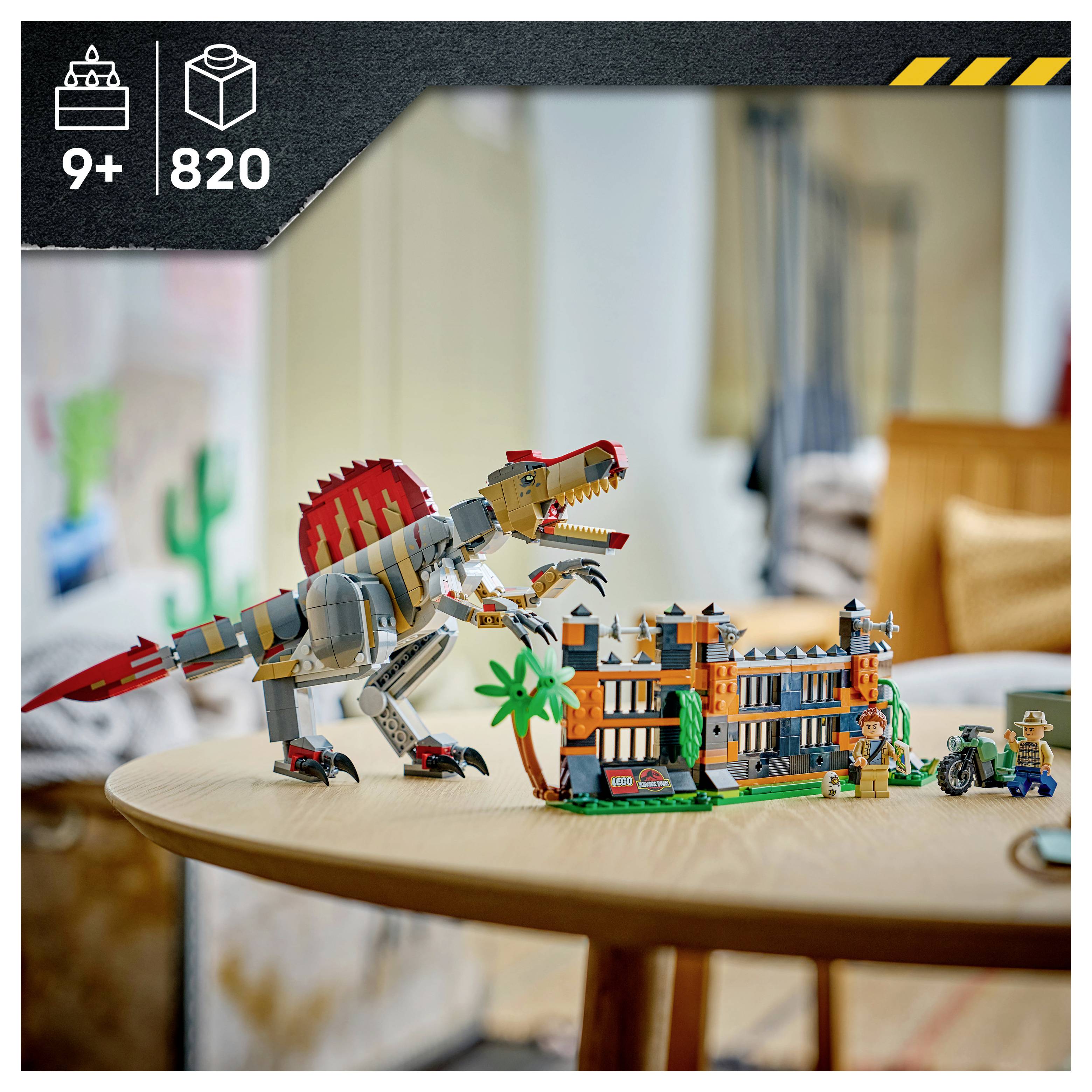 LEGO-Dinosaurier-Set auf einem Tisch, mit einem T-Rex neben einem mehrstöckigen Gebäude und Minifiguren; die Schachtelillustration zeigt Altersangabe 9+ und 820 Teile.