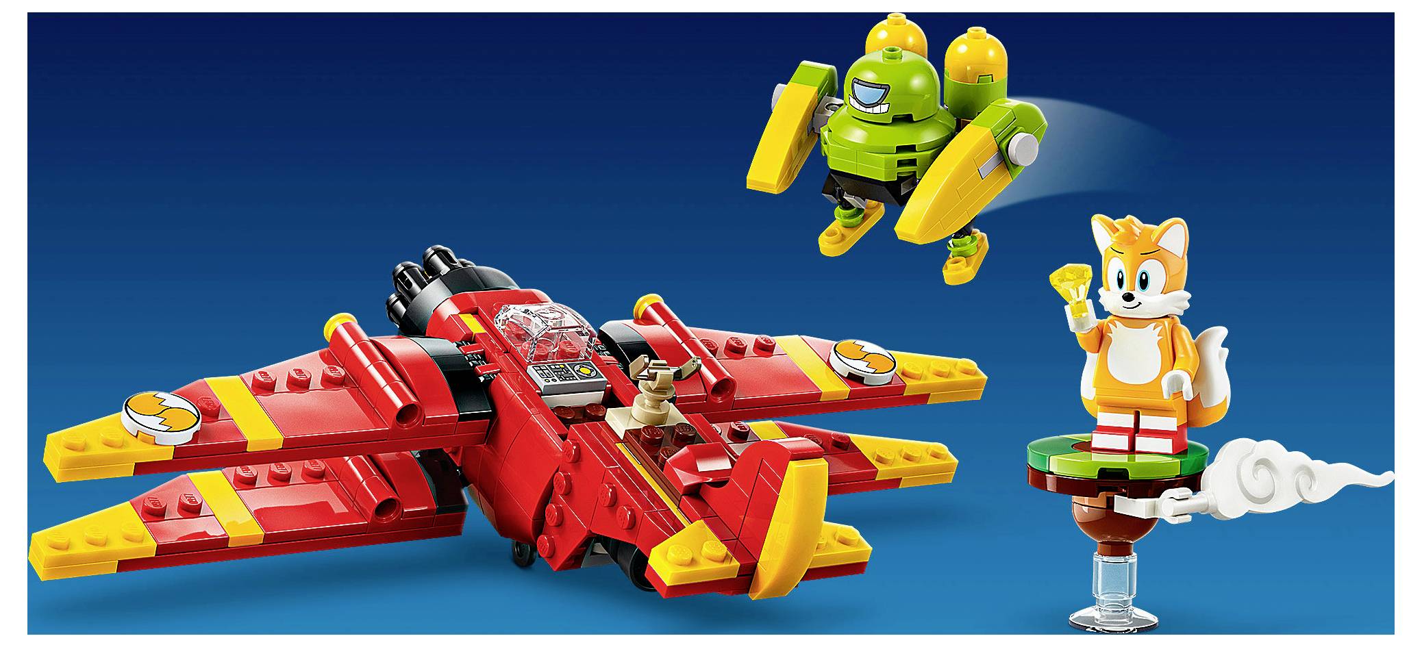 Ein LEGO-ähnlicher roter Jet mit einem Piloten, ein grüner Roboter fliegt darüber, und Tails steht auf einer kleinen Plattform, alles vor einem blauen Hintergrund dargestellt.