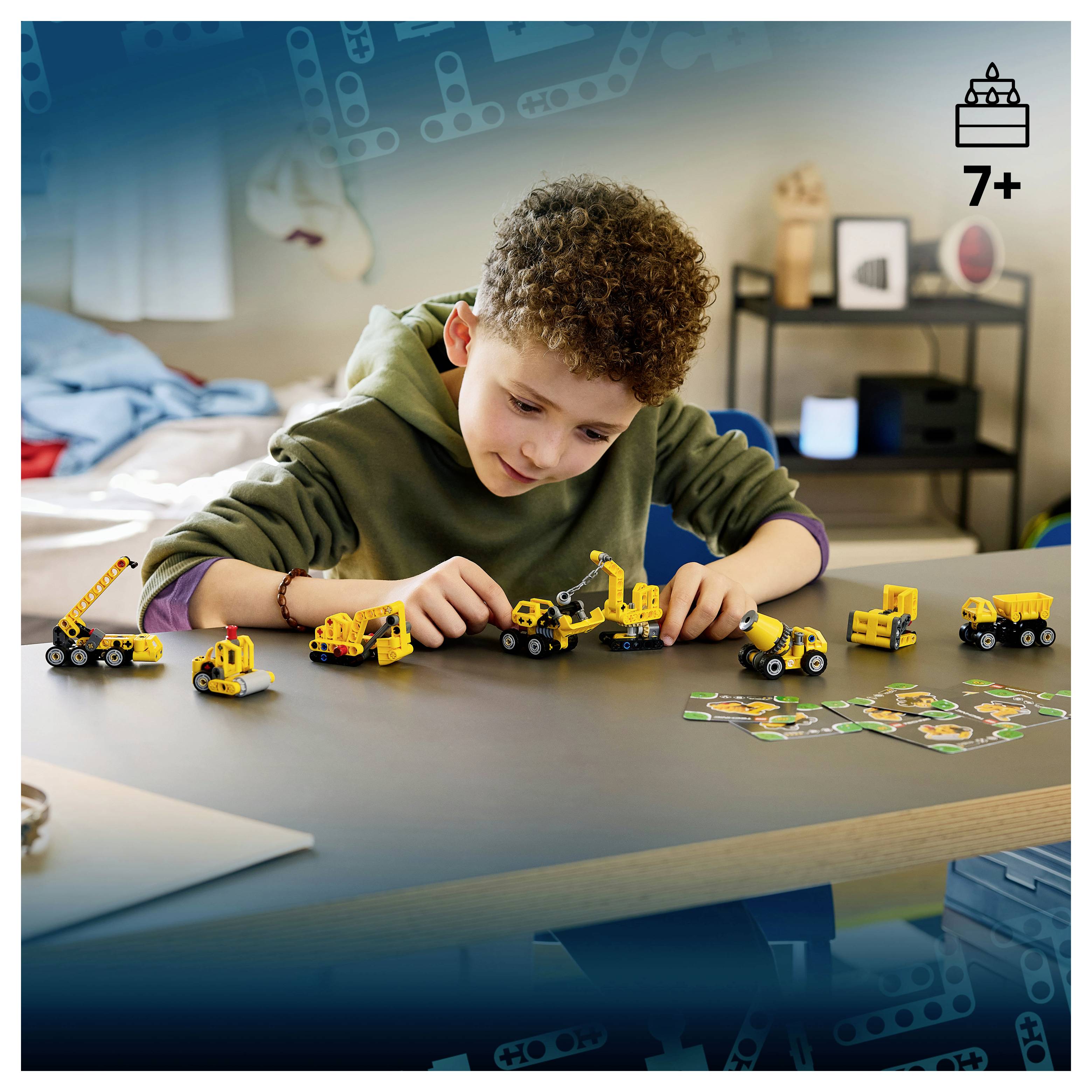 Ein kleiner Junge spielt mit kleinen gelben Spielzeugfahrzeugen zum Bauen auf einem Tisch; ein „7+