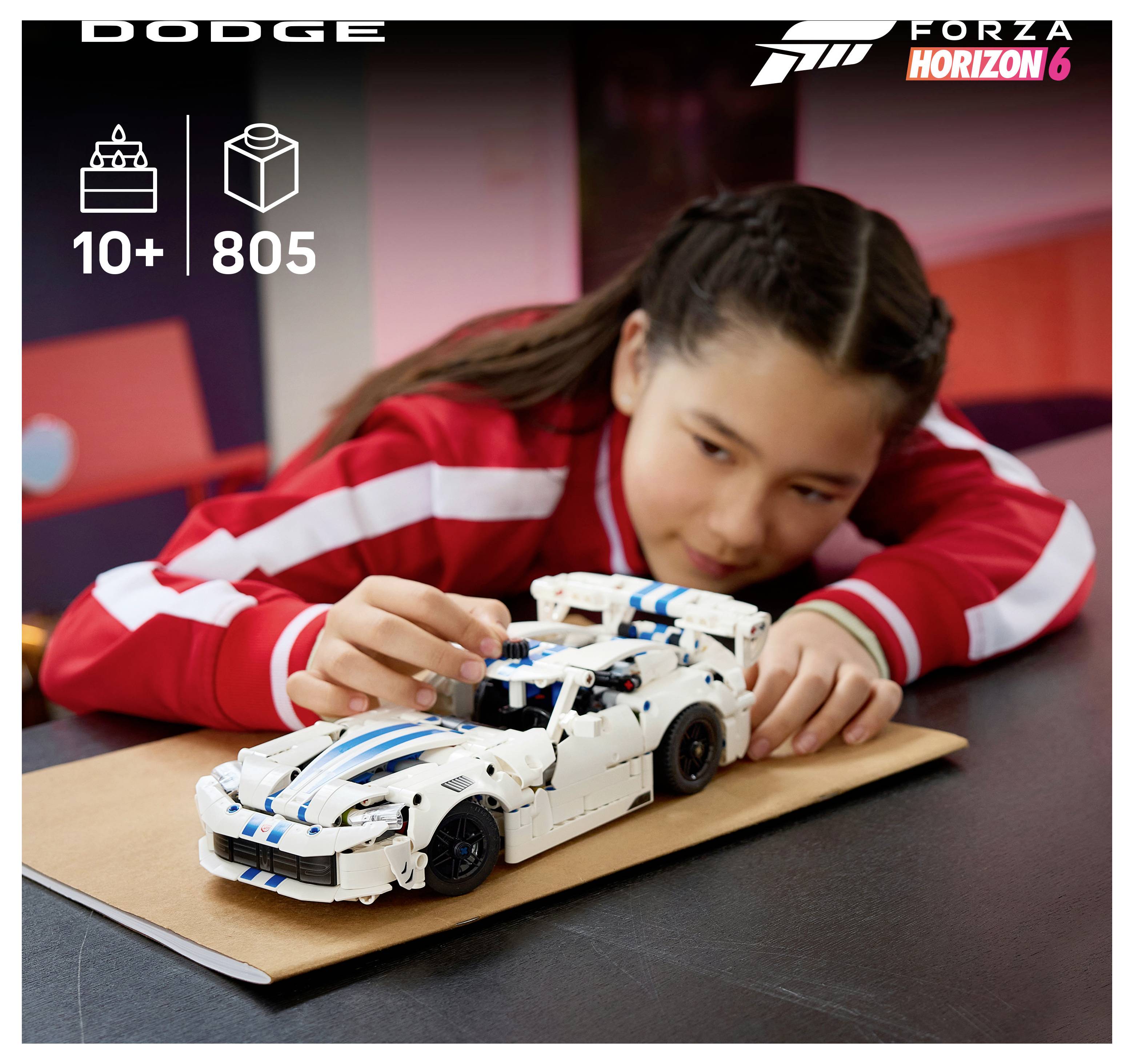 Mädchen in einer roten Jacke baut auf einem Tisch ein weißes Dodge-Rennwagen-LEGO-Modell zusammen; „DODGE