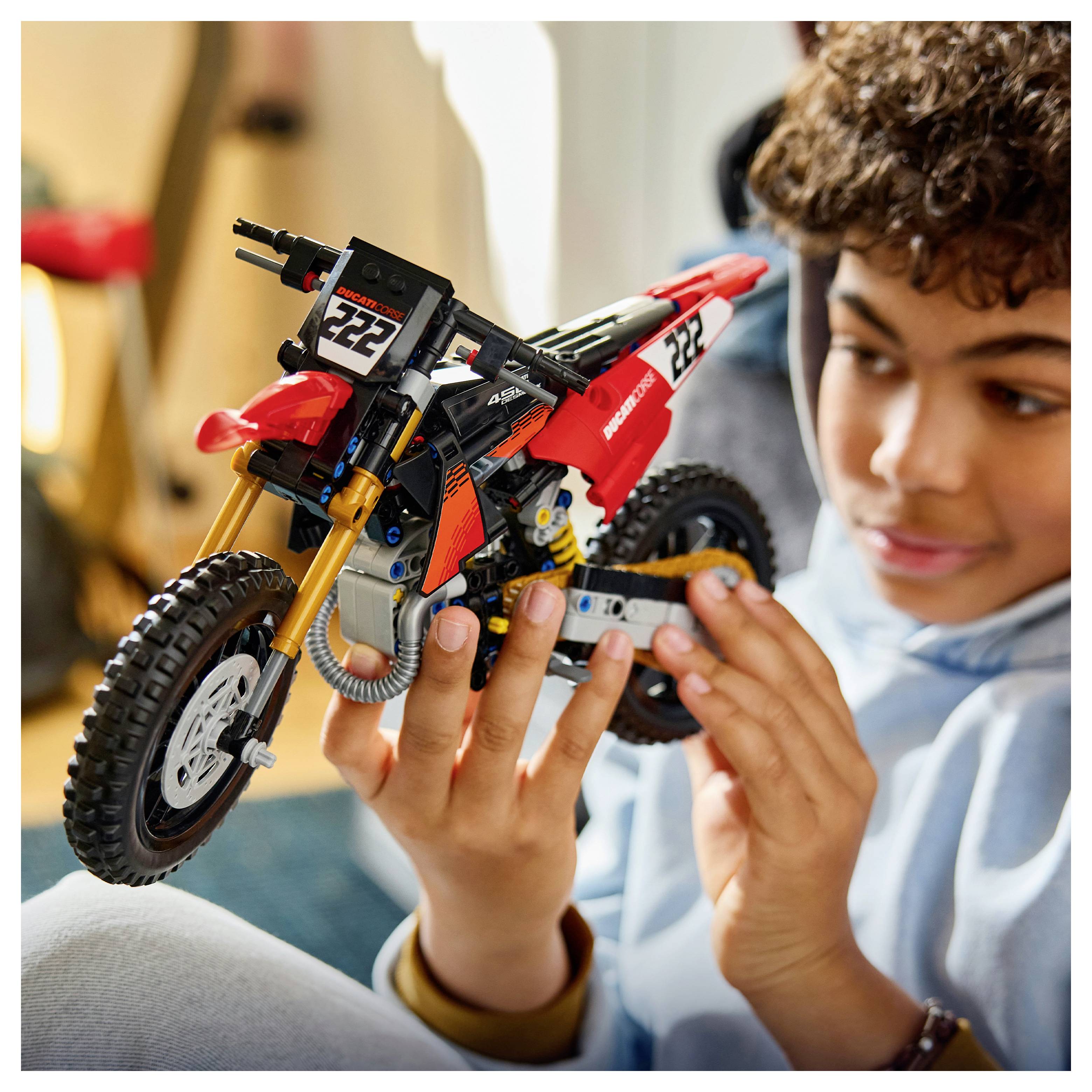 Ein Junge untersucht ein rot-schwarzes Spielzeug-Motocross-Motorrad und hält es vorsichtig in seinen Händen.