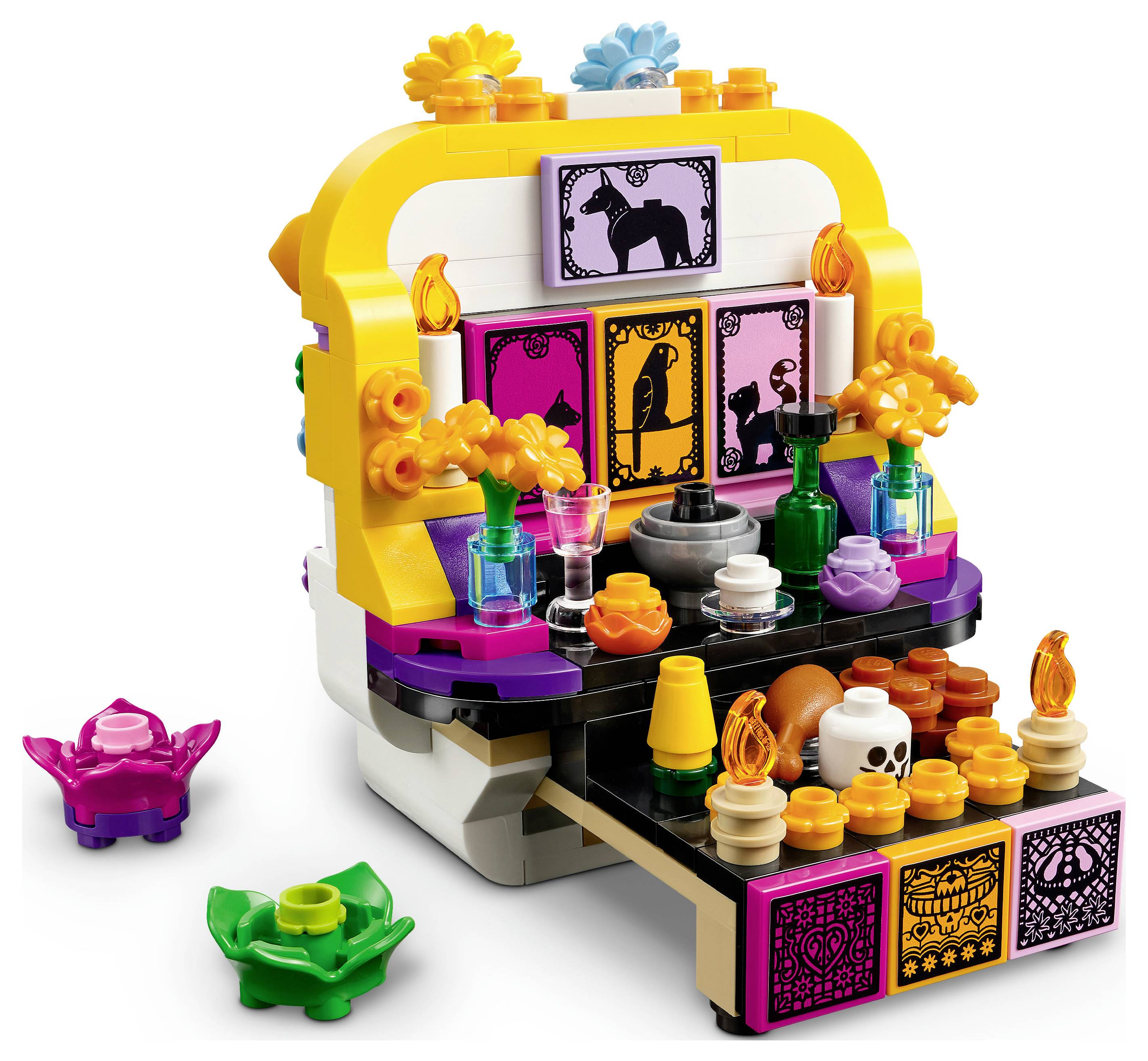 Farbenfroher LEGO-ähnlicher Miniaturaltar mit Tiersillhouetten-Kacheln, Kerzen, Blumen, Getränken, Totenschädel und Lebensmitteln auf einem schwarz-gelben Ausstellungsständer.